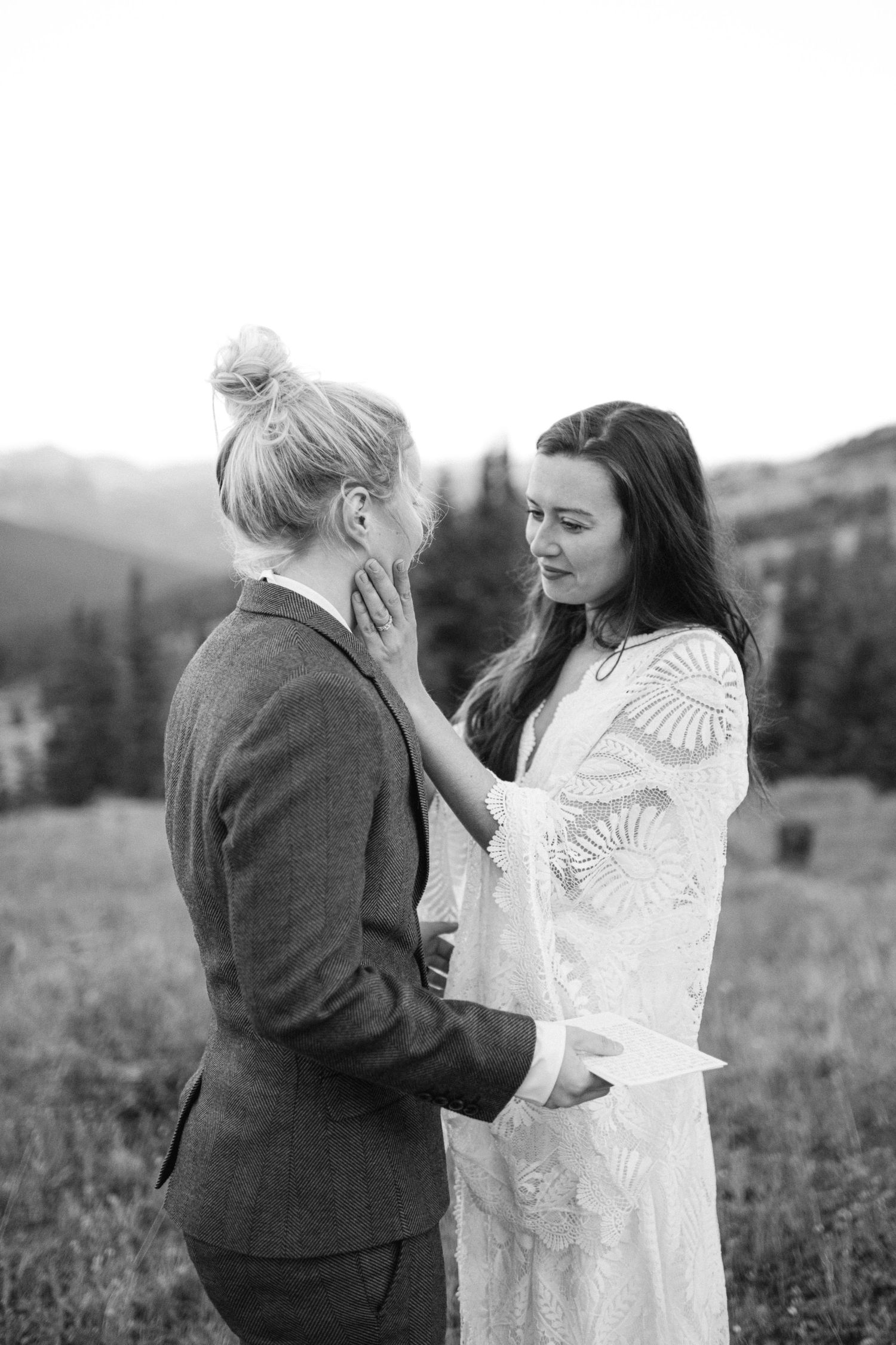 Black and white intimate moment captured between two people in mountain meadow setting.