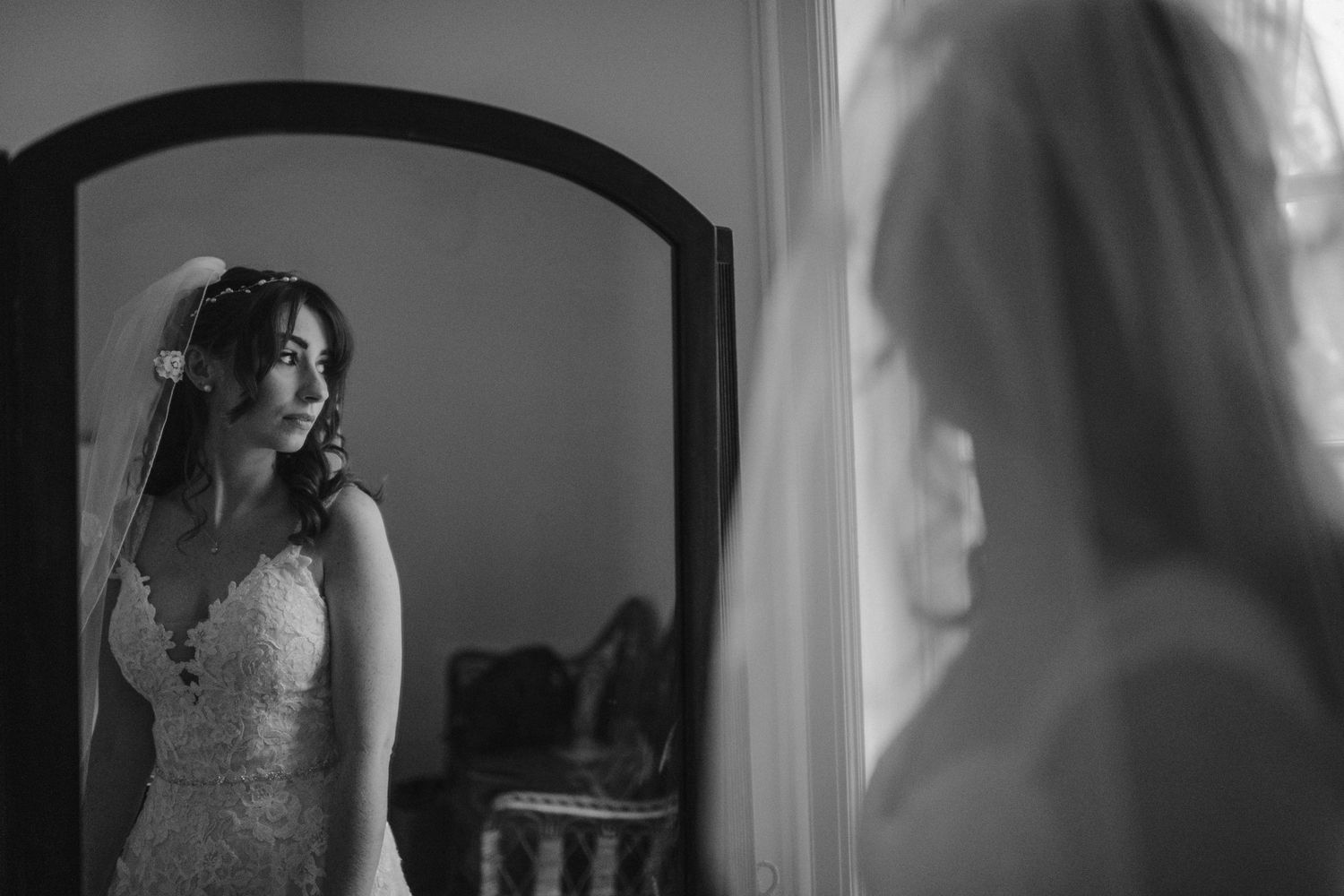 Dramatic black and white portrait of bride looking in mirror during wedding preparations.