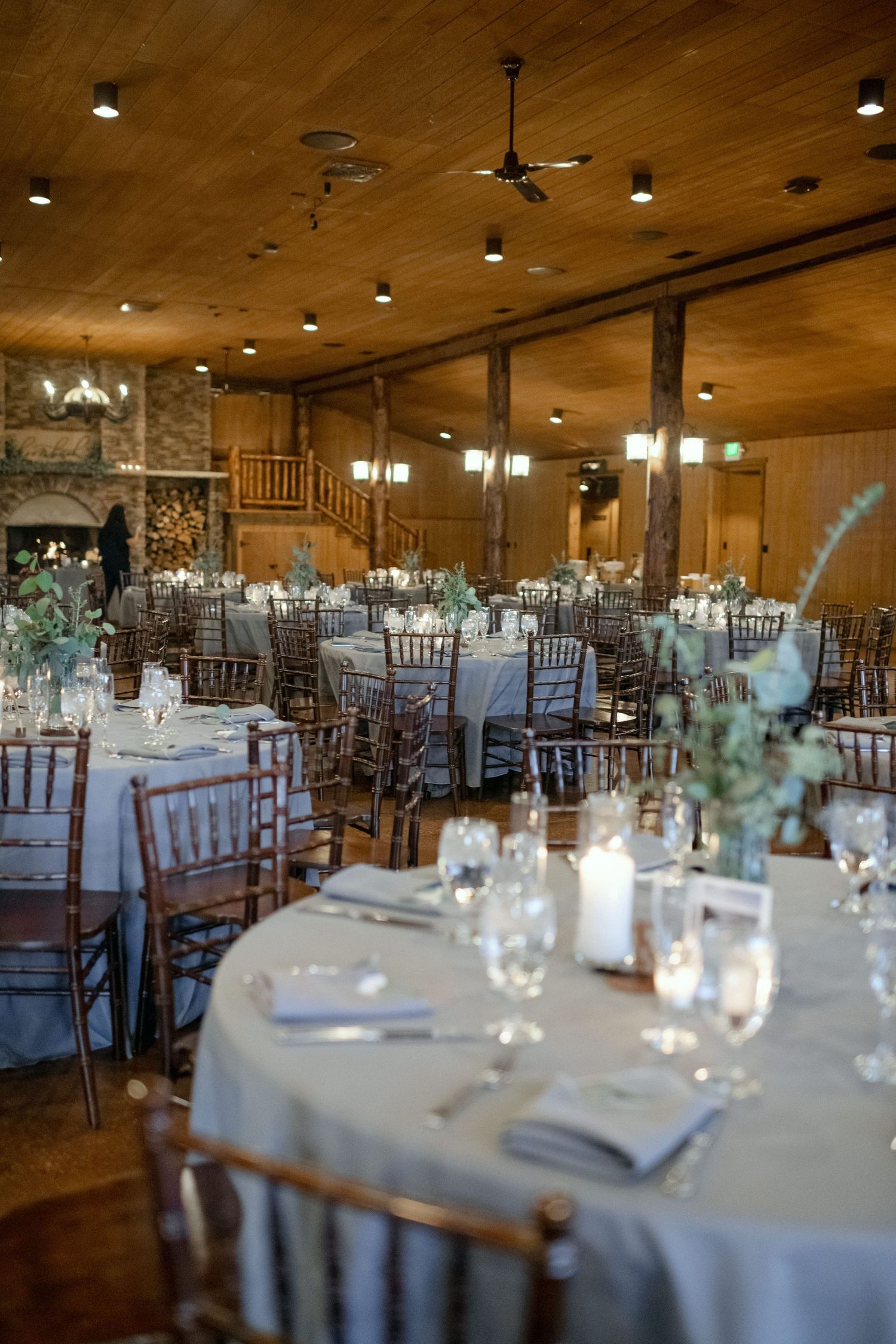 Rustic wedding reception venue with wooden ceiling, stone fireplace, and elegant table settings.