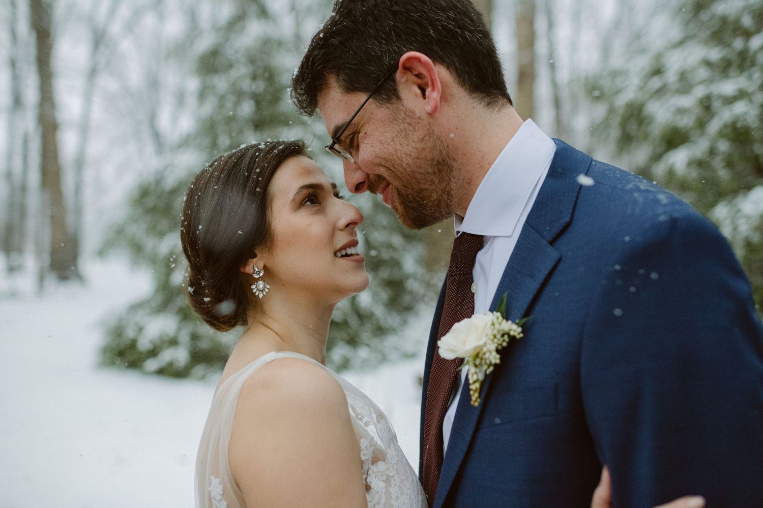 A romantic winter wedding moment with snow falling in a forest setting.