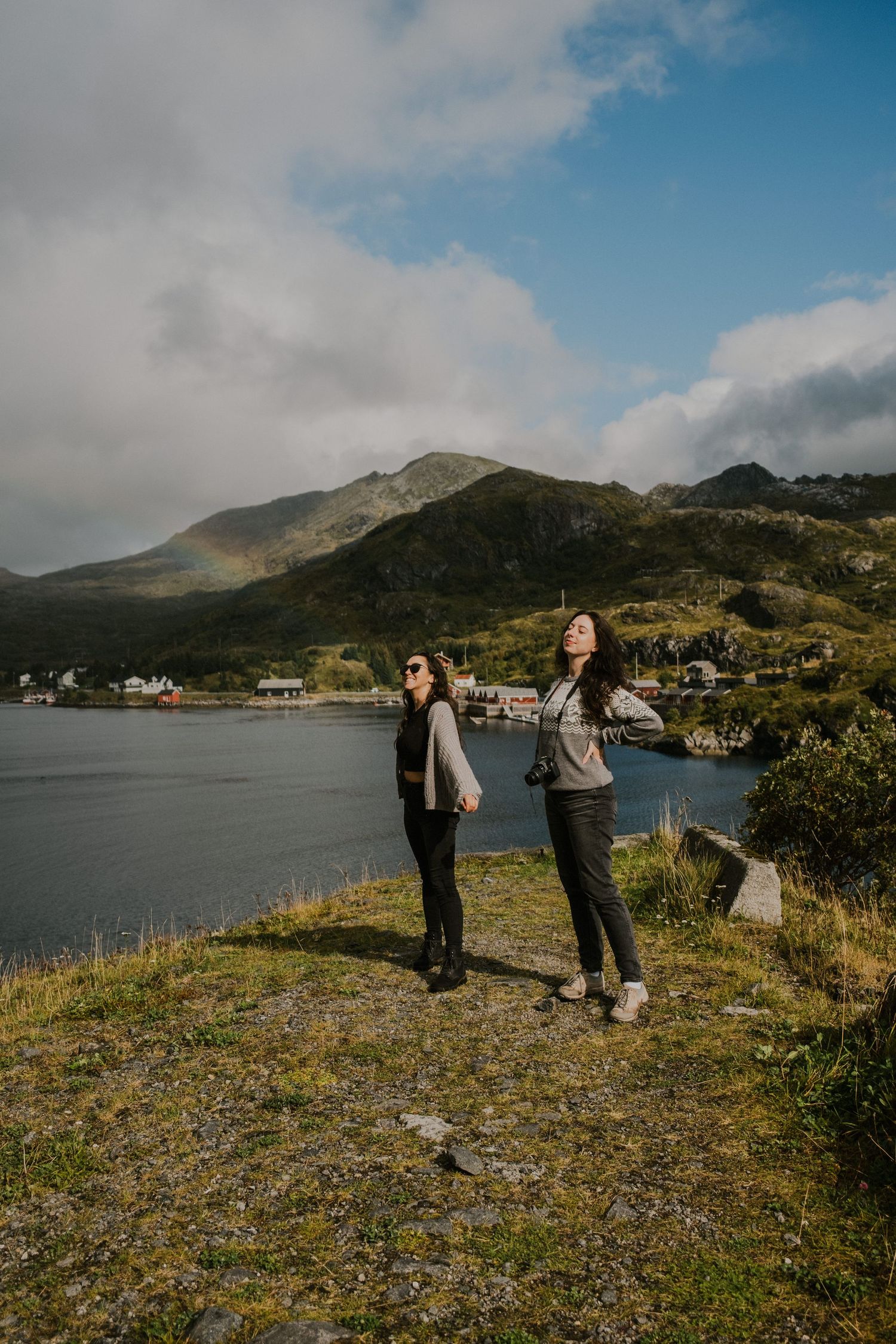 Scenic overlook of a coastal village nestled between mountains and fjord under partly cloudy skies.