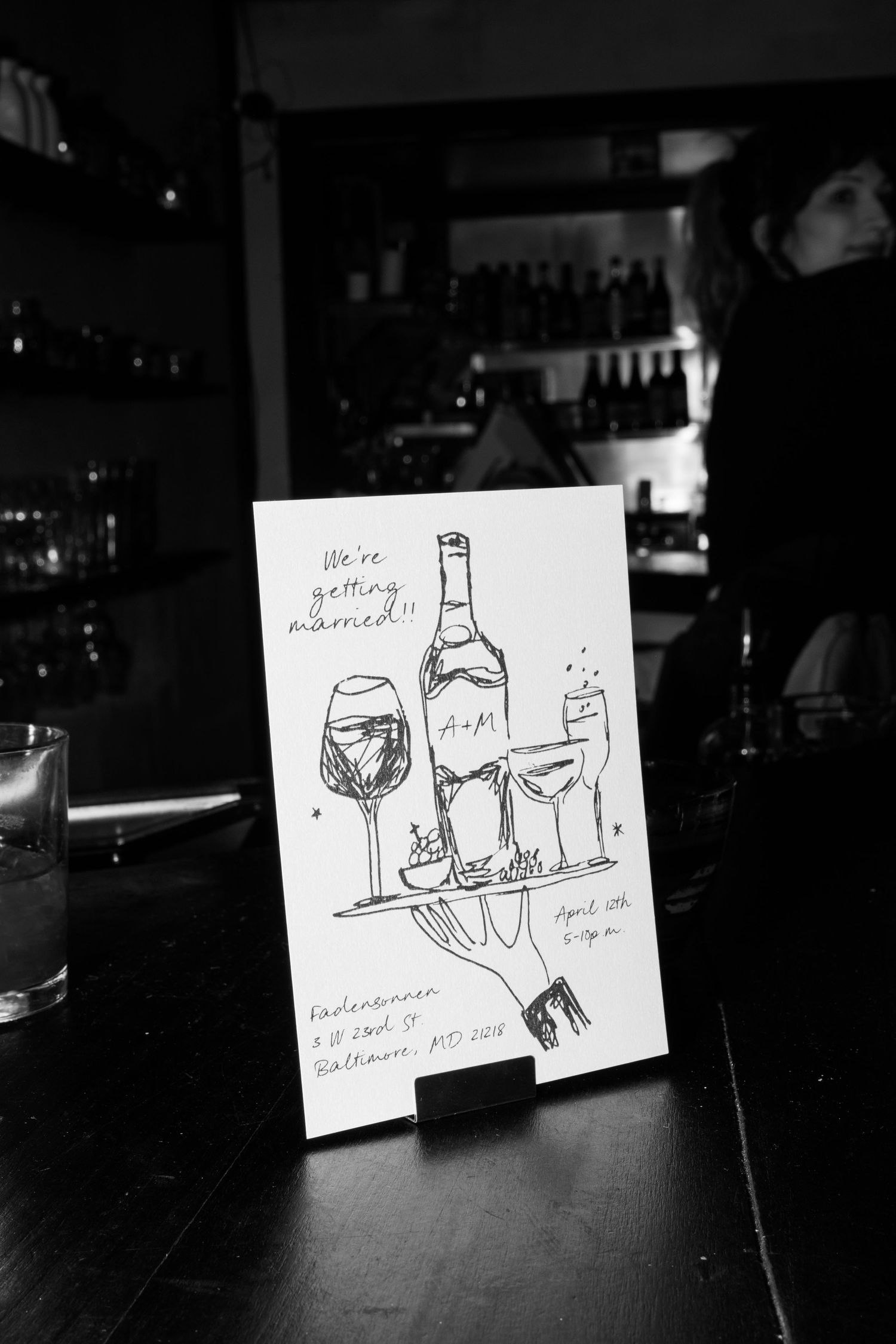 A black and white sketch of wine glasses and bottles displayed on a bar counter.