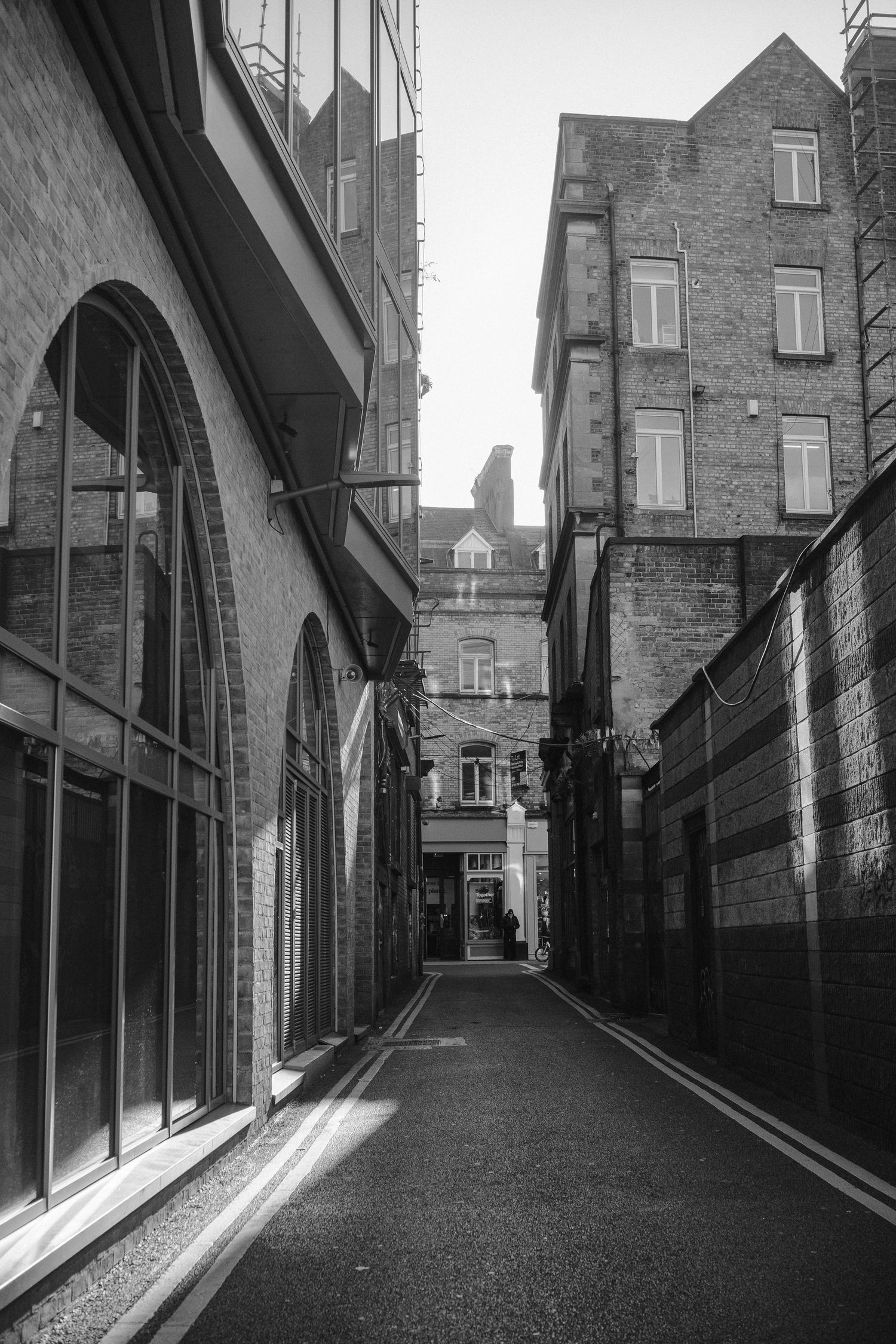 Narrow alley between brick buildings with arched windows in black and white.