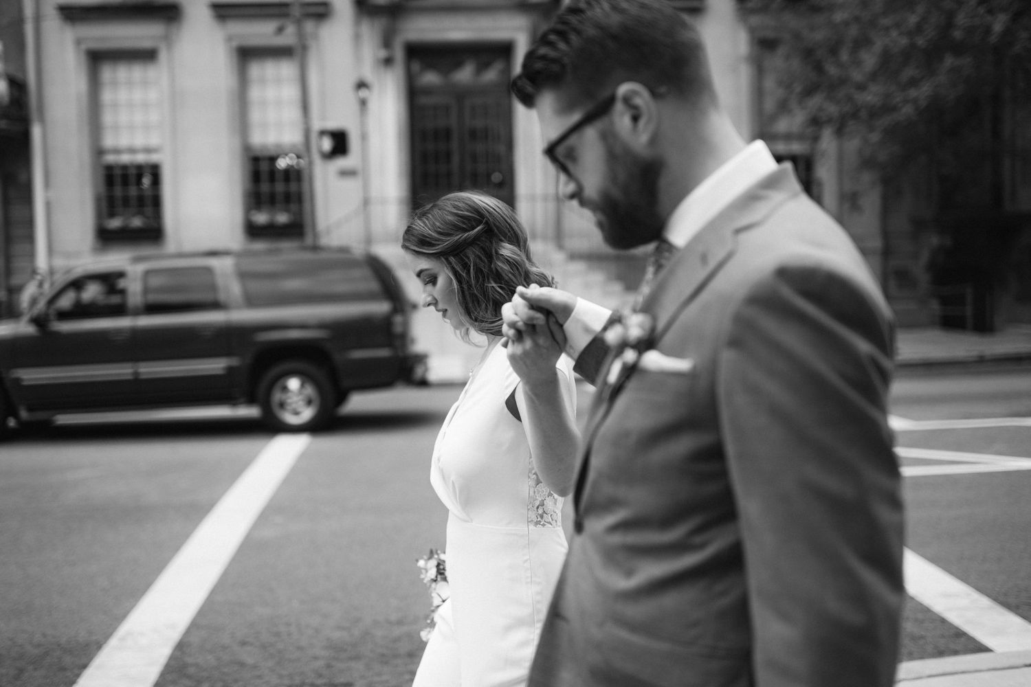 Urban black and white wedding moment showing a couple looking at a phone on a city street.