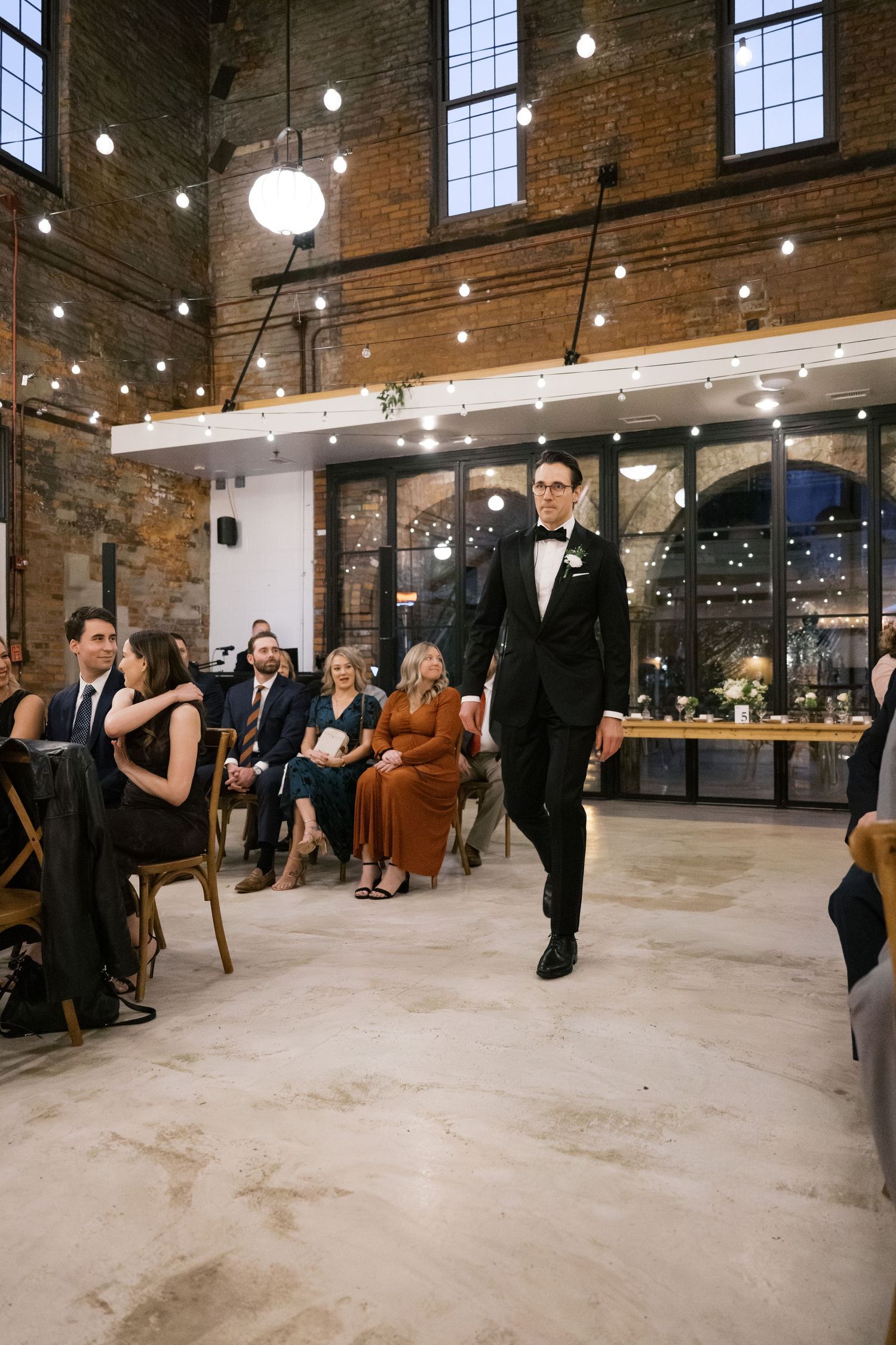 A formal event in an industrial-chic venue with exposed brick walls, pendant lights and elegantly dressed attendees.
