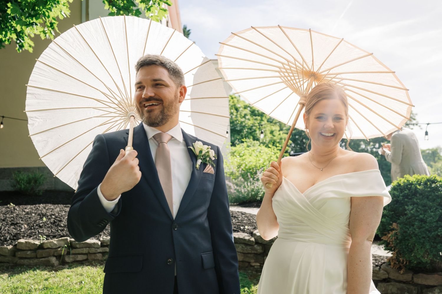 Couple poses with white parasols during their sunny outdoor wedding.