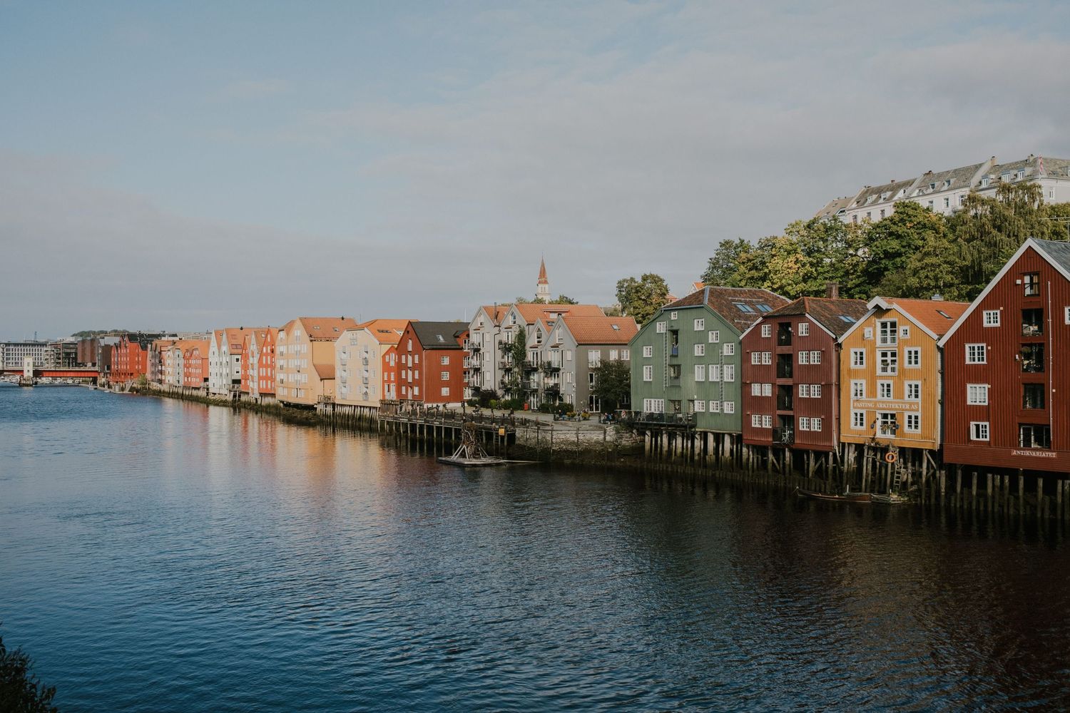 Row of colorful wooden buildings reflecting in calm harbor waters under cloudy sky.