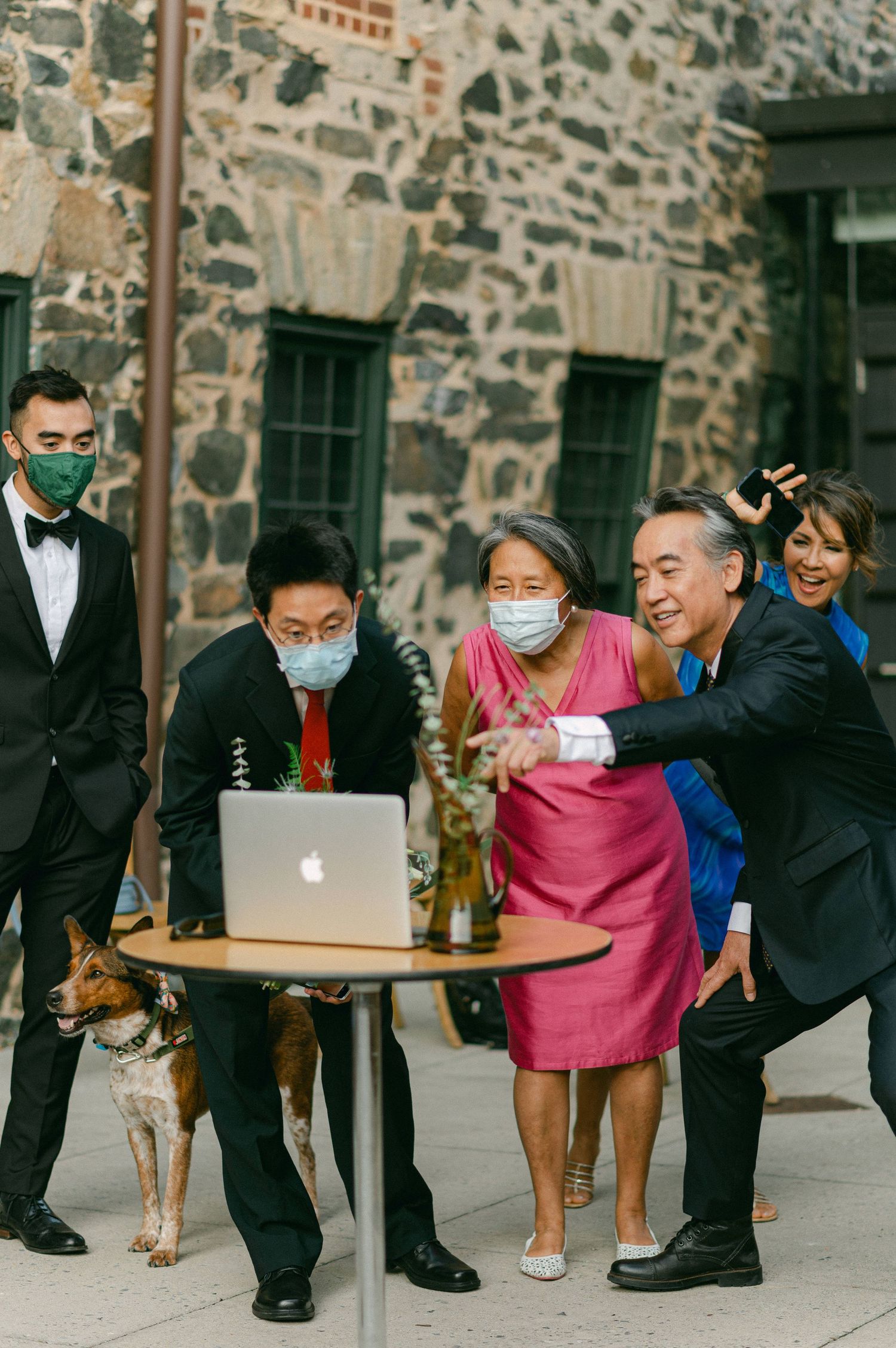 family crowds around laptop as guests join for the wedding ceremony on Zoom
