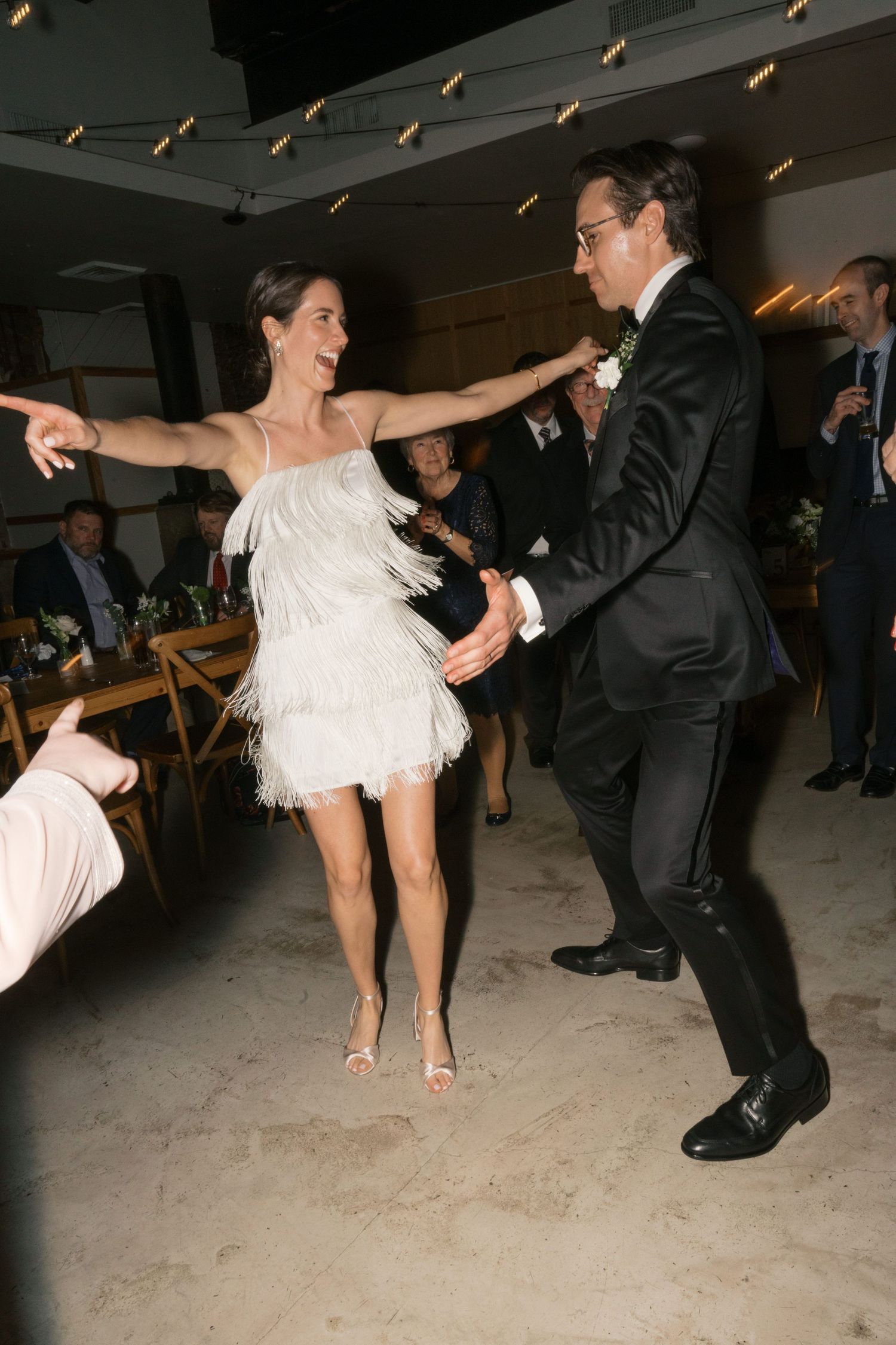 A joyous dance moment at a celebration with two people swinging in a decorated indoor venue.