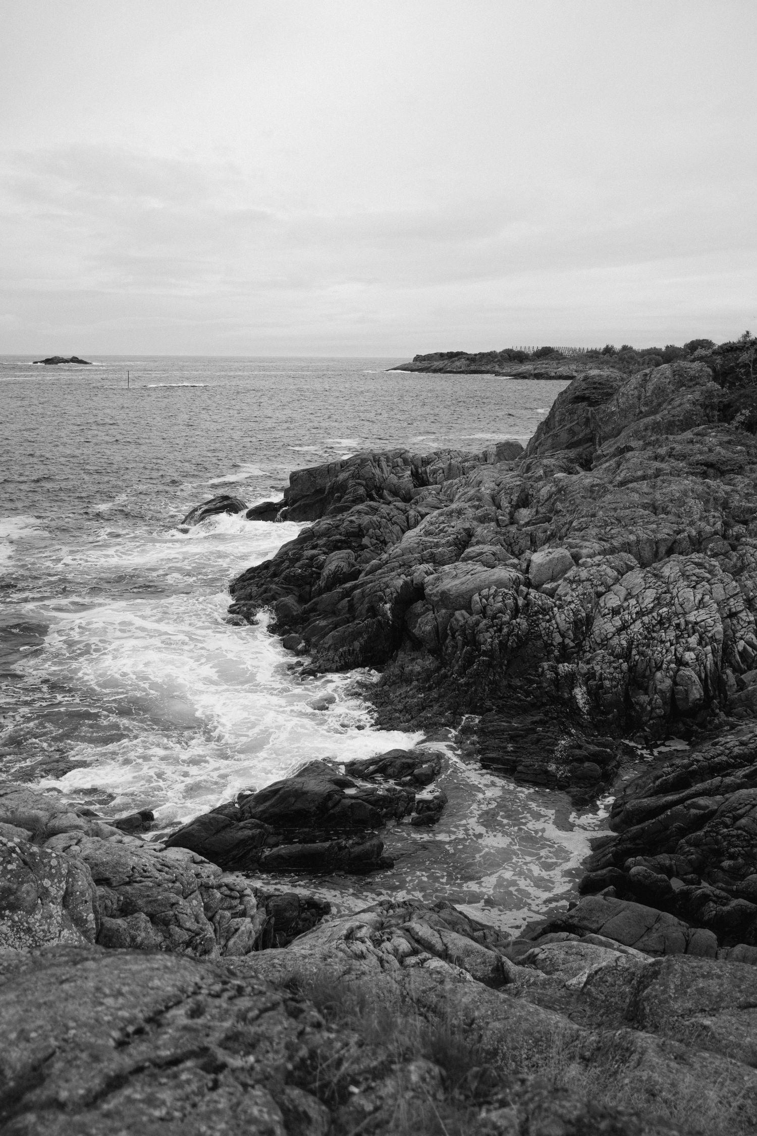 Dramatic black and white coastal scene with waves crashing against rocky cliffs.