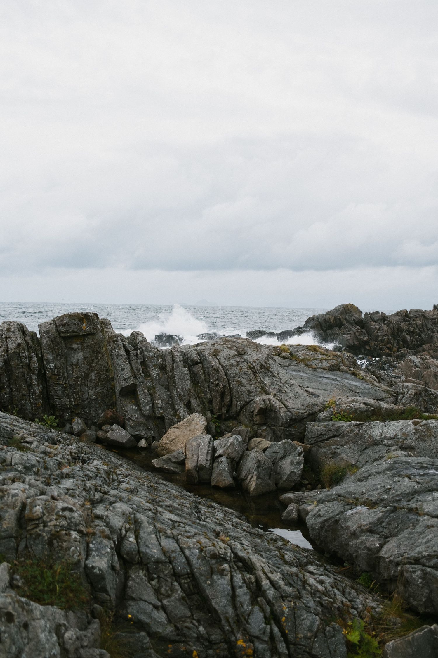 Waves crash against rugged coastal rocks under overcast sky in moody seascape.