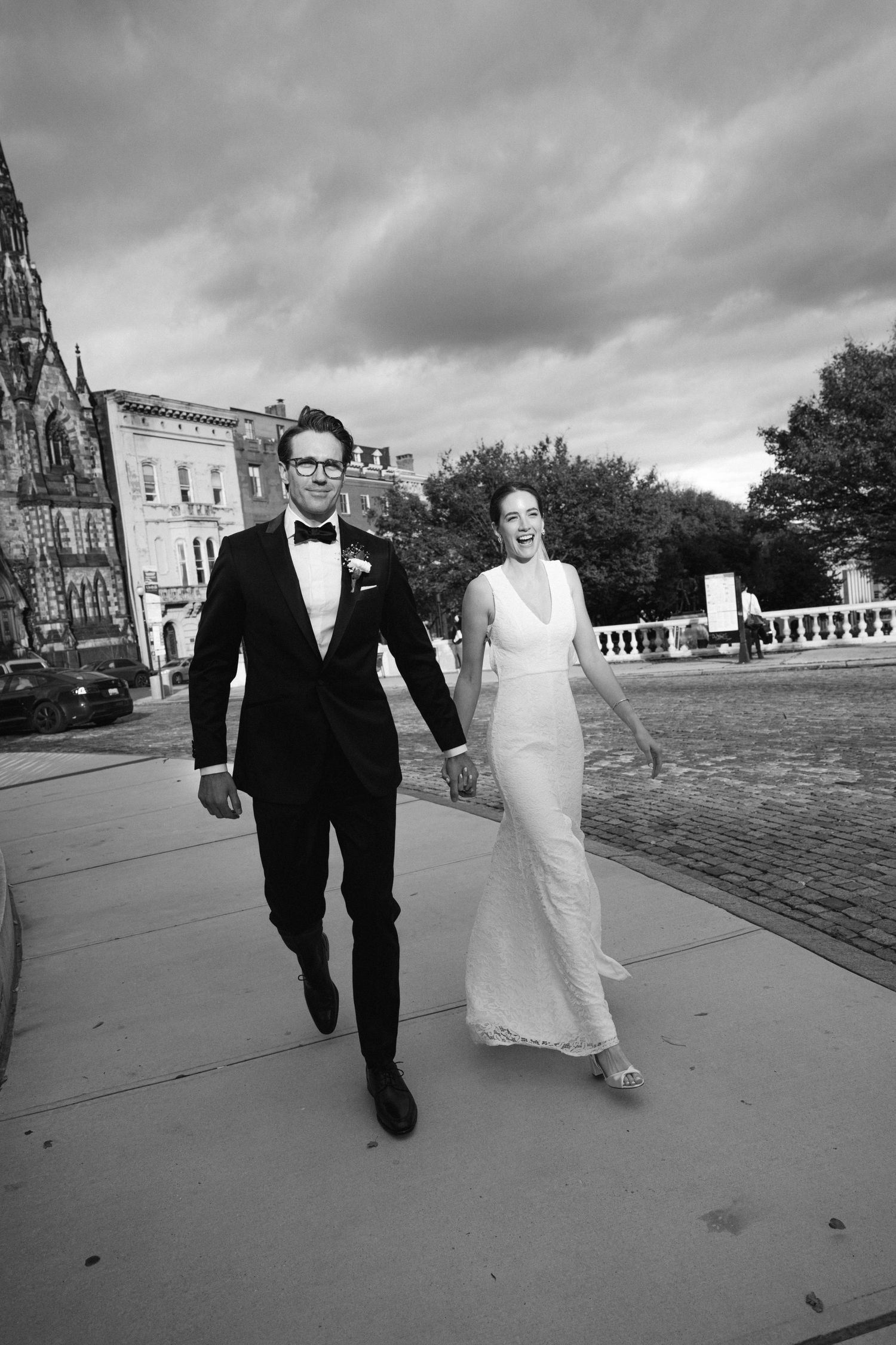 Black and white photo of couple walking on city street in formal wedding attire.