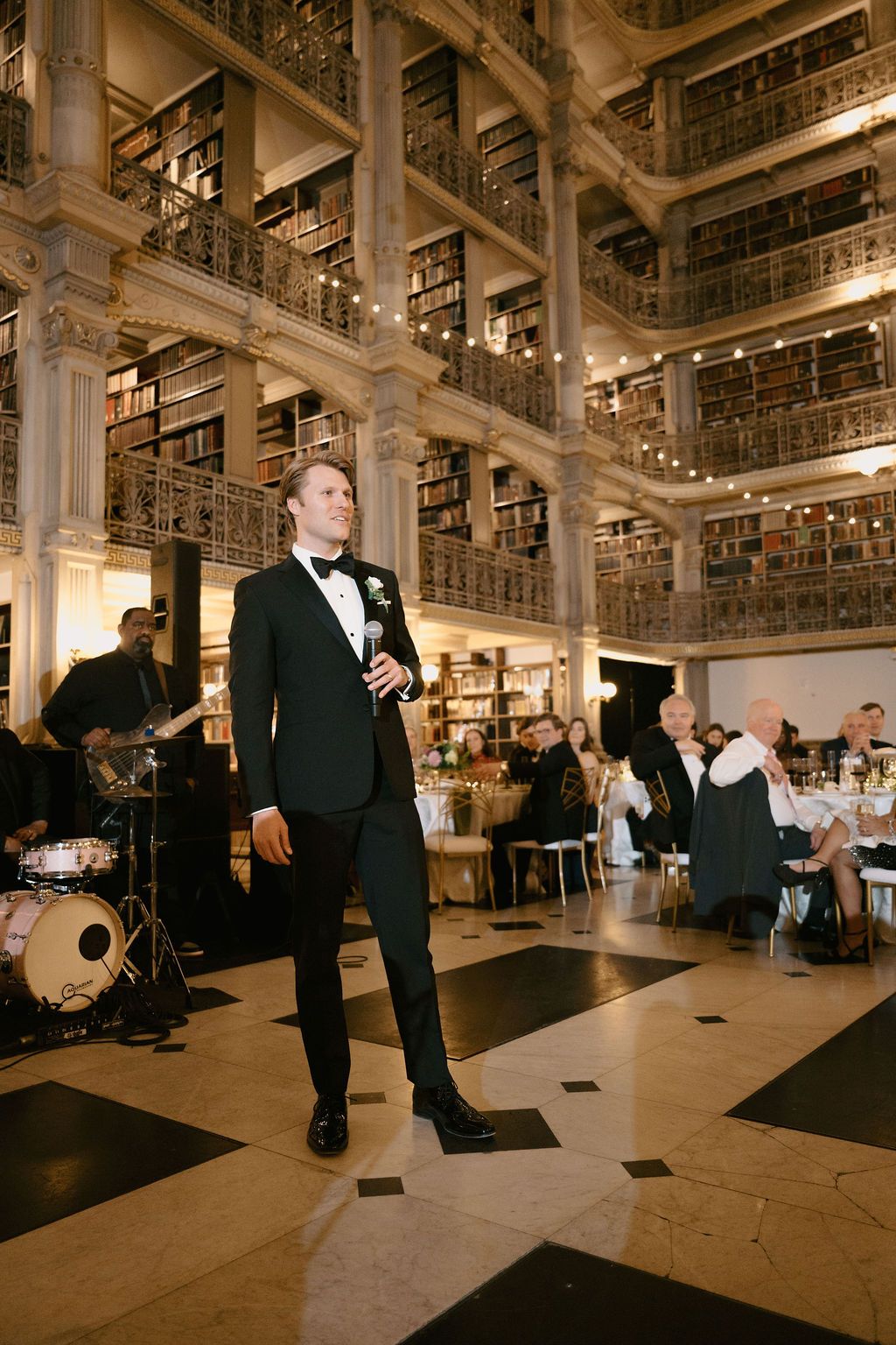 Musicians perform at an elegant wedding reception in a grand historic library venue with ornate architecture.