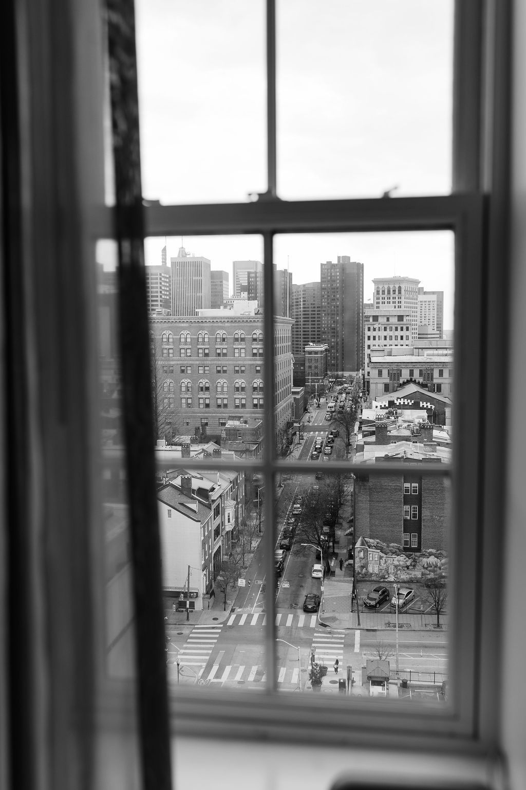 Black and white cityscape view through window showing urban buildings and streets.