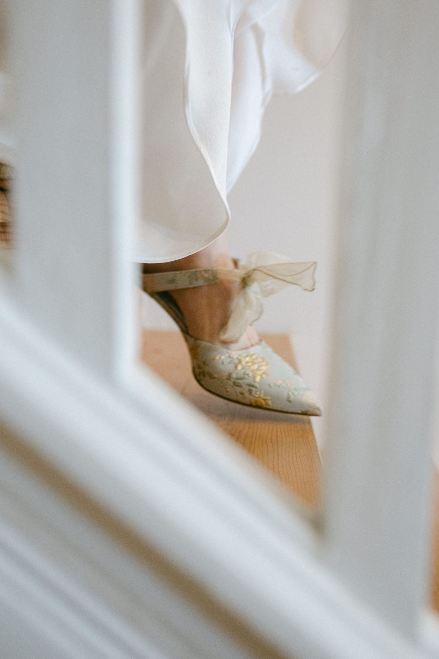 Close-up detail of white wedding shoes seen through decorative railings.