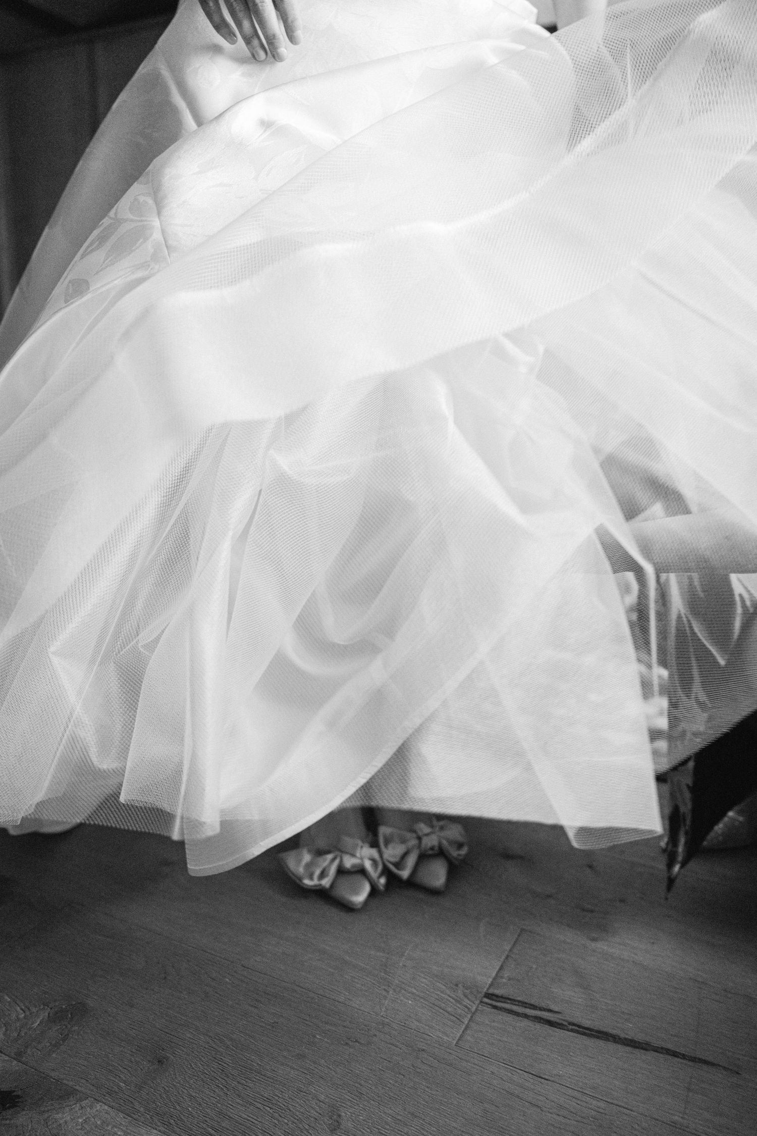 Close-up details of flowing white tulle wedding dress fabric against dark flooring.