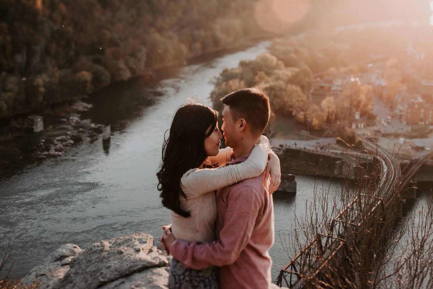 Romantic couple embracing on clifftop overlooking river valley at sunset.
