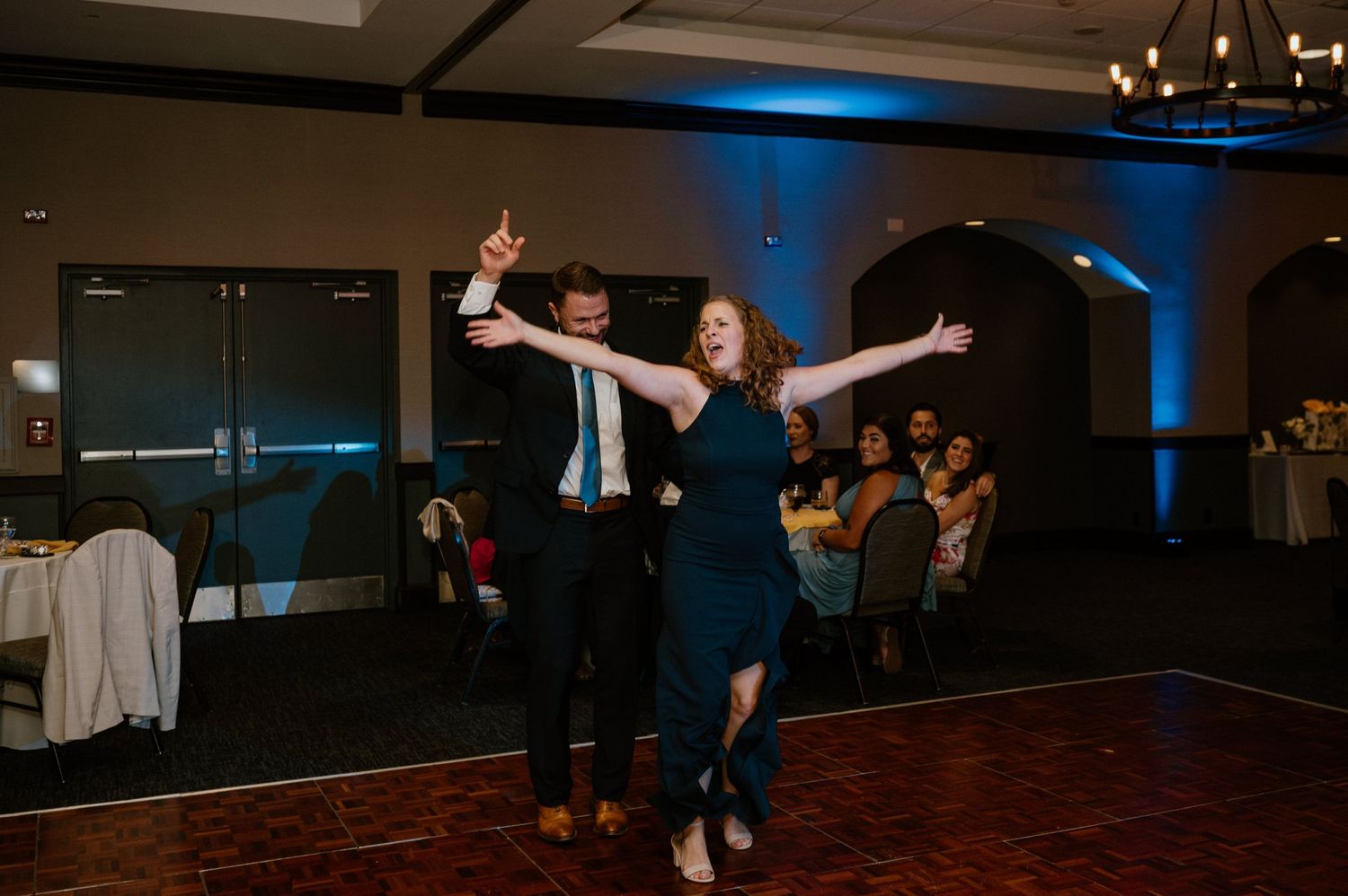 Couple performing energetic dance moves on wooden floor at evening reception.