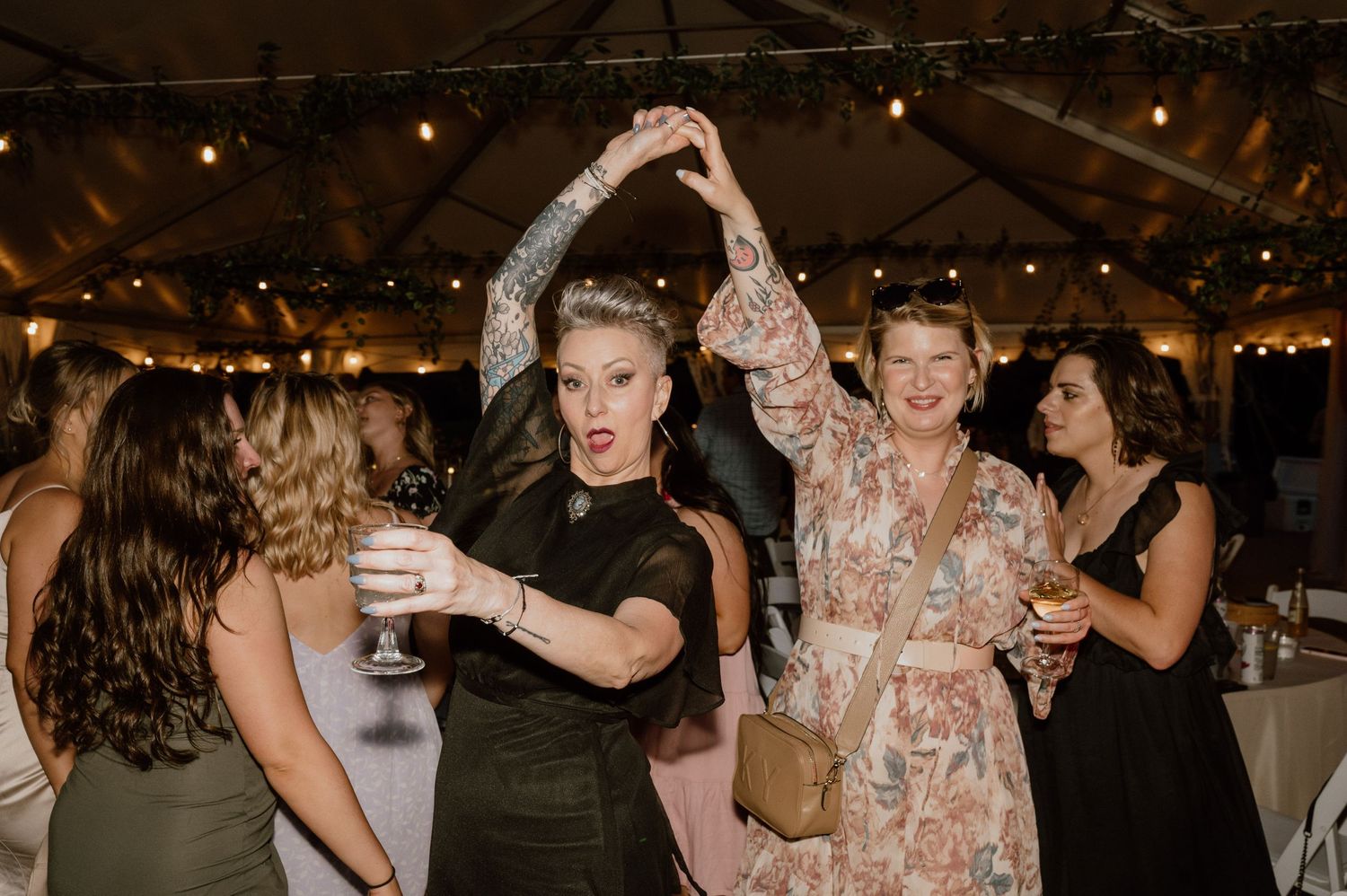 Wedding guests dancing and twirling under string lights at an evening reception.