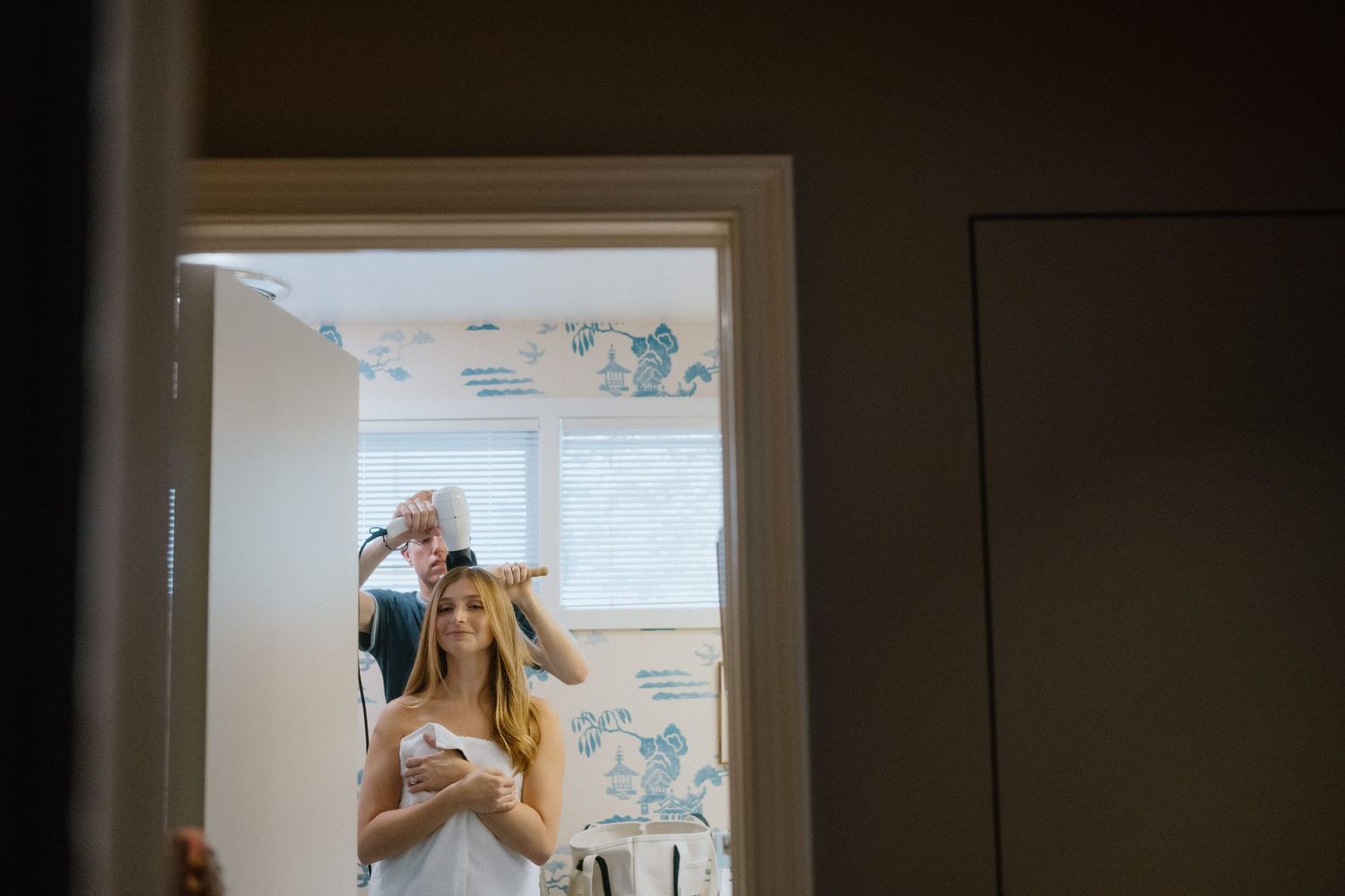 A tender moment between two people in a bathroom with floral wallpaper in the background.