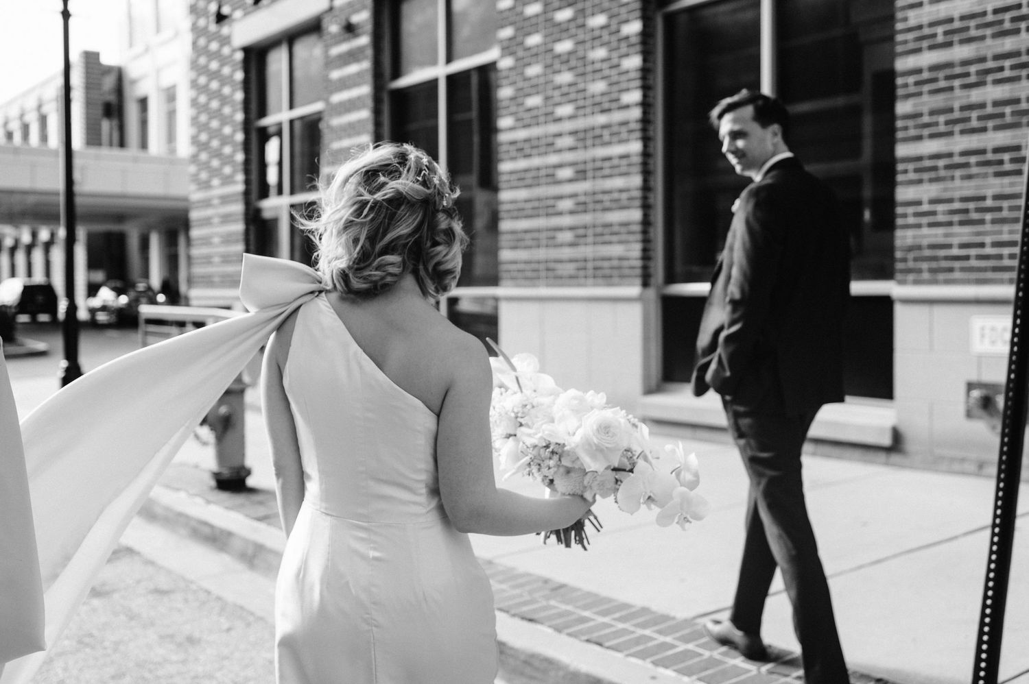 Black and white photo of wedding couple having first look moment on city street.