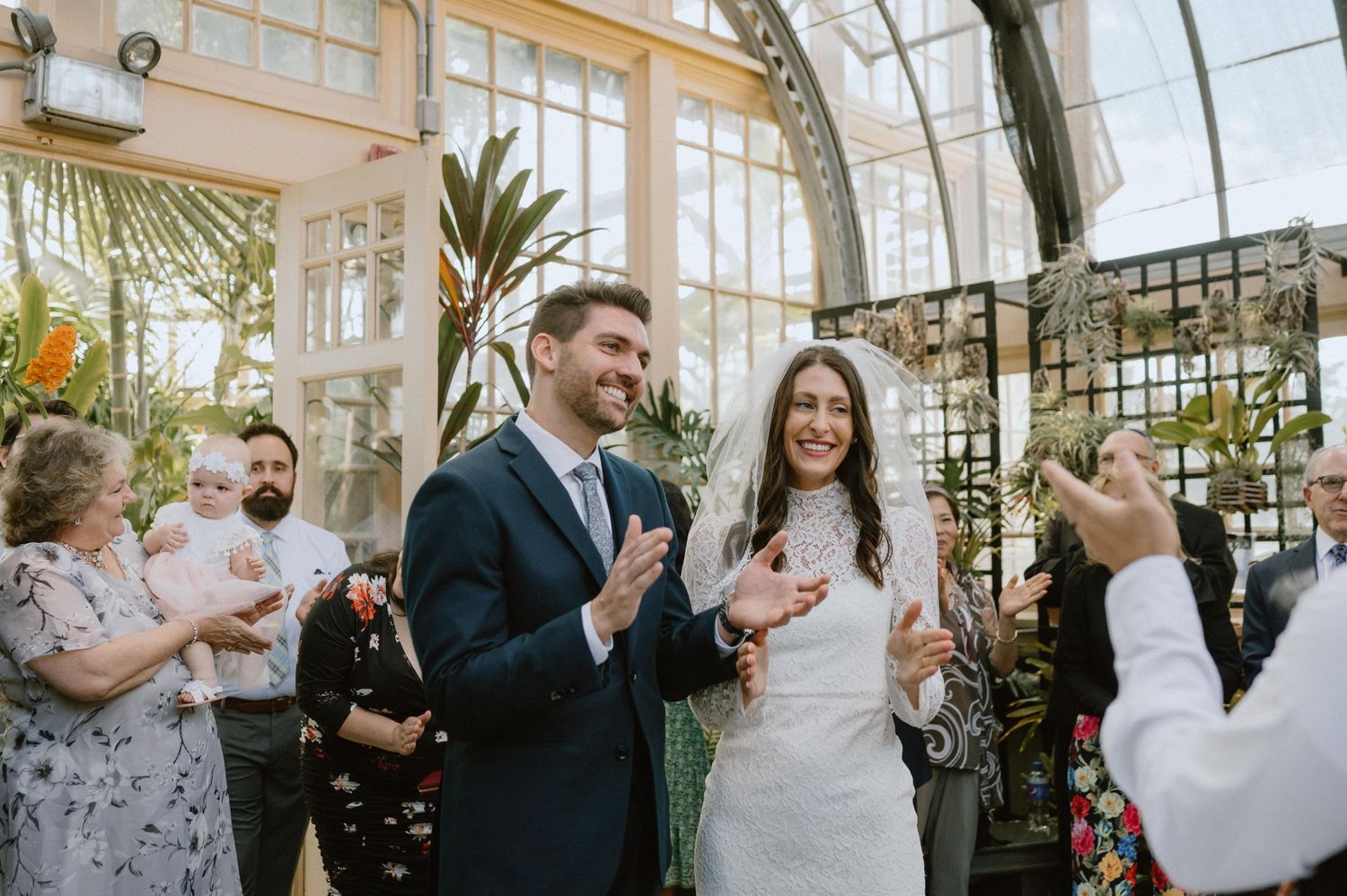 Joyful celebration moment during a wedding ceremony in a light-filled greenhouse.
