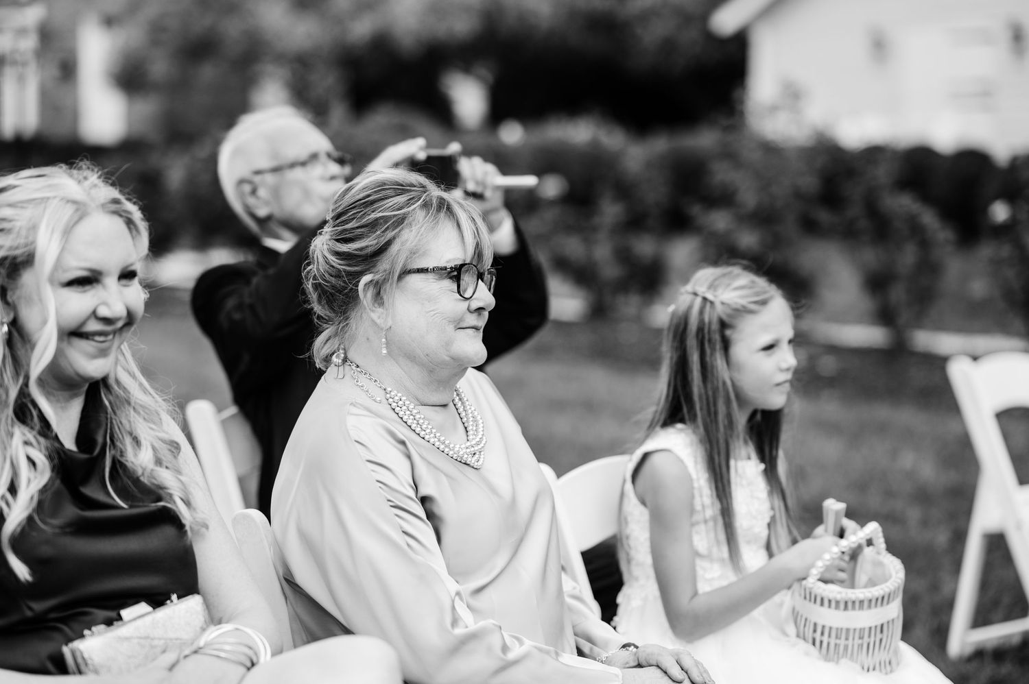 Black and white photo of wedding guests laughing and clapping during outdoor reception.