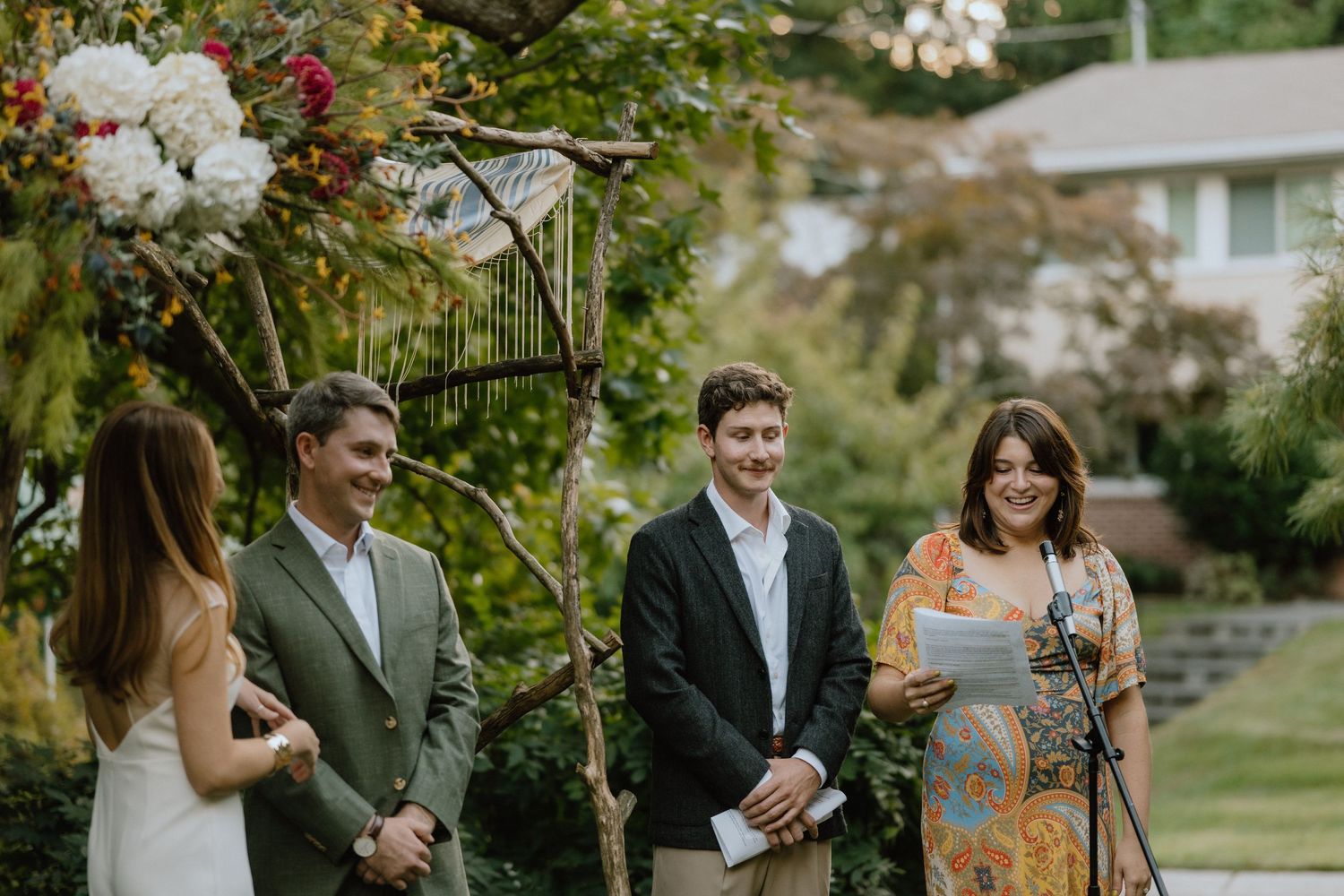 Outdoor wedding ceremony under a floral arch with red and white blooms.