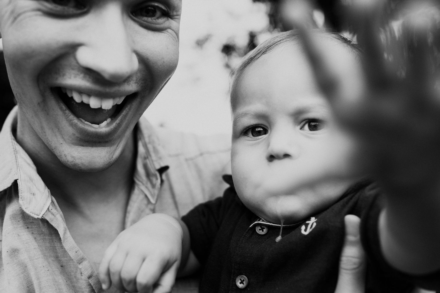 Black and white candid photo of parent and baby sharing a playful moment.