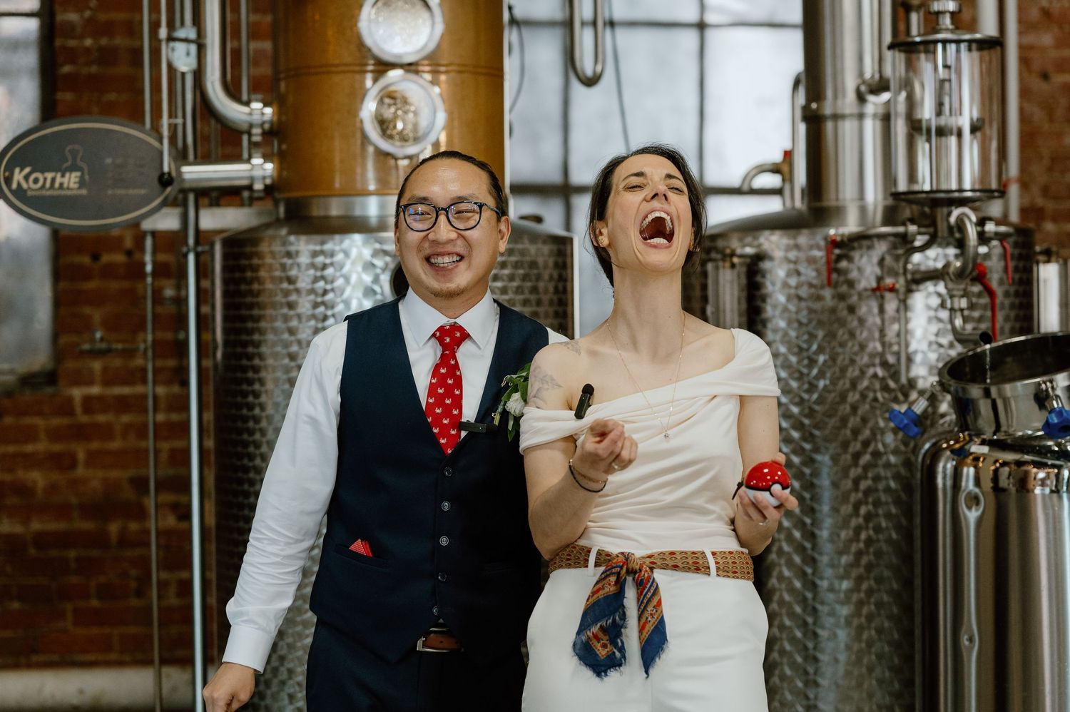 Couple sharing a joyful moment among distillery equipment and brick walls.