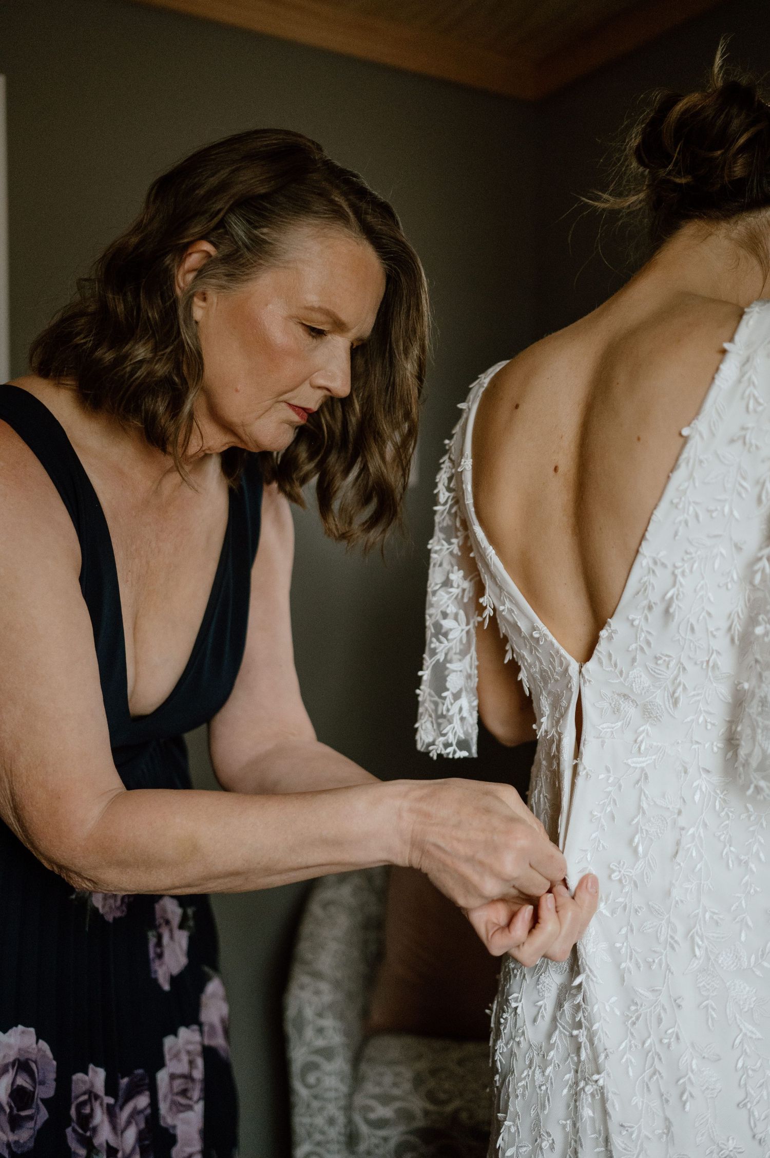 Helper assisting with the fastening of a detailed lace wedding gown.