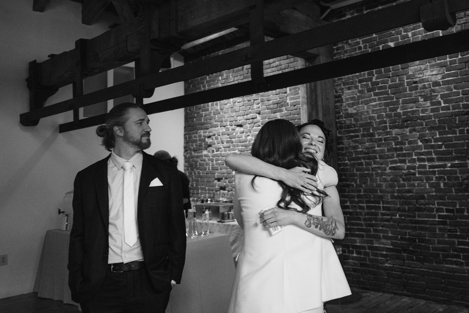 A black and white candid moment at a wedding reception with exposed brick walls.
