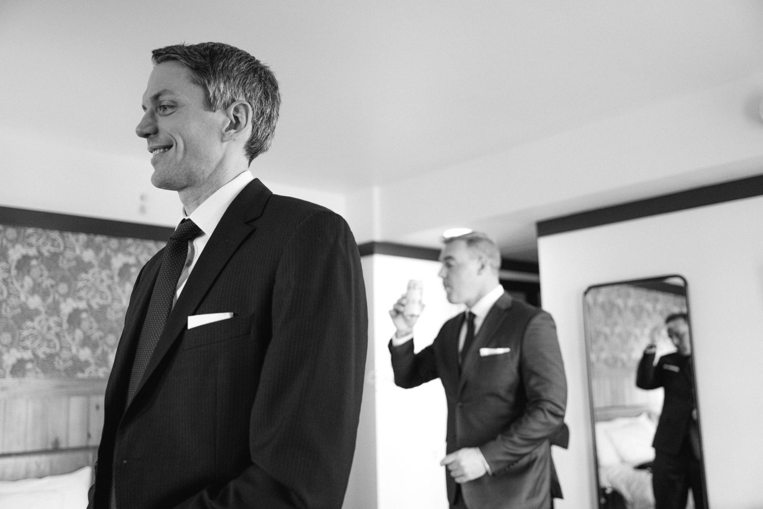 Black and white photo of a suited figure smiling while others prepare in the background.