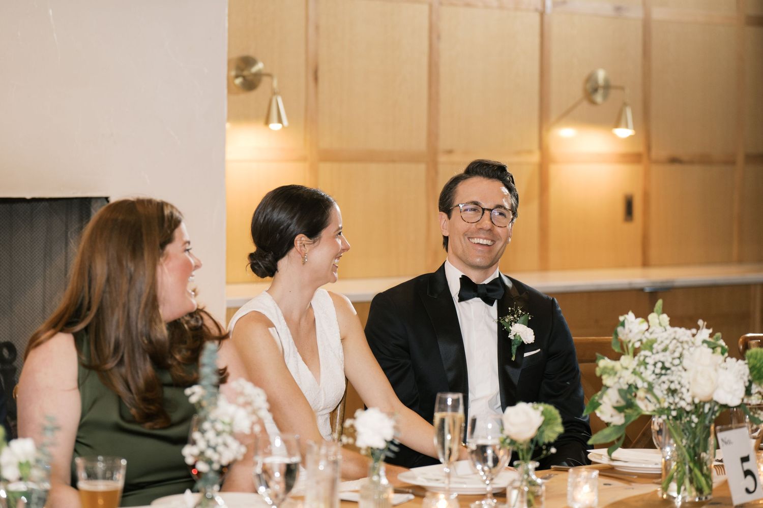Event attendees enjoying conversation and drinks at an elegant reception dinner table decorated with white floral centerpieces.