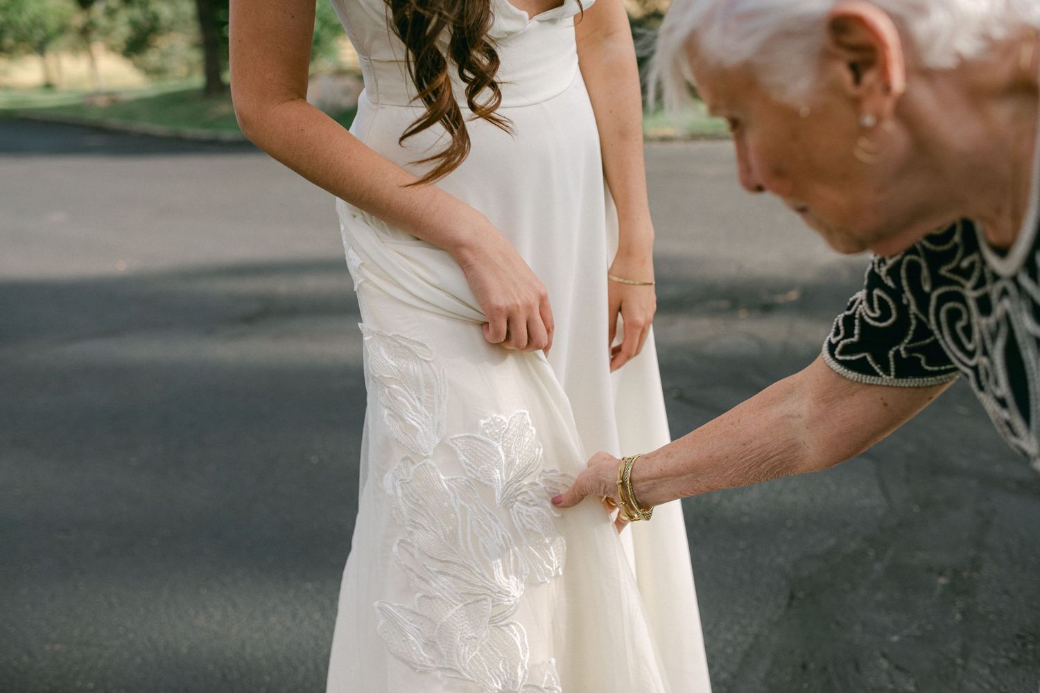 Close-up of wedding dress being adjusted outdoors.