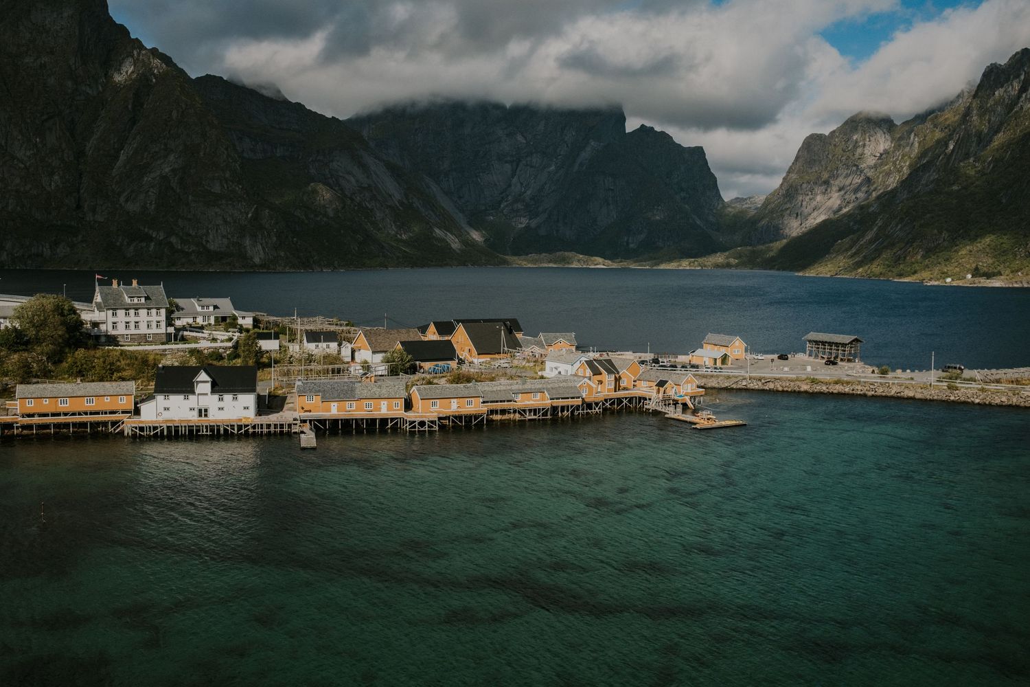 Scenic view of Norwegian fishing village with traditional buildings along harbor surrounded by steep mountains.
