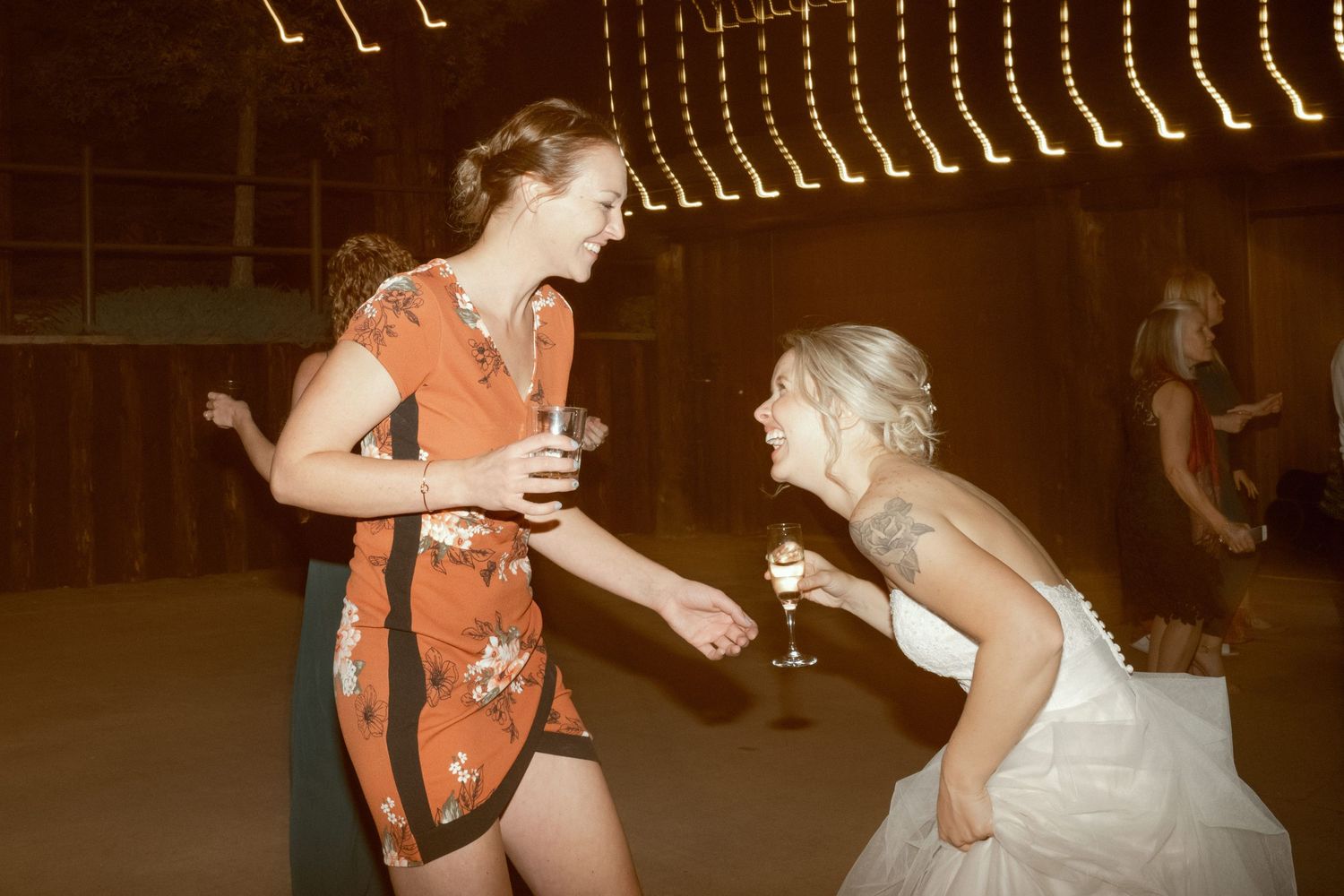 A candid moment at a wedding reception shows dancers interacting on the dance floor under warm lighting.