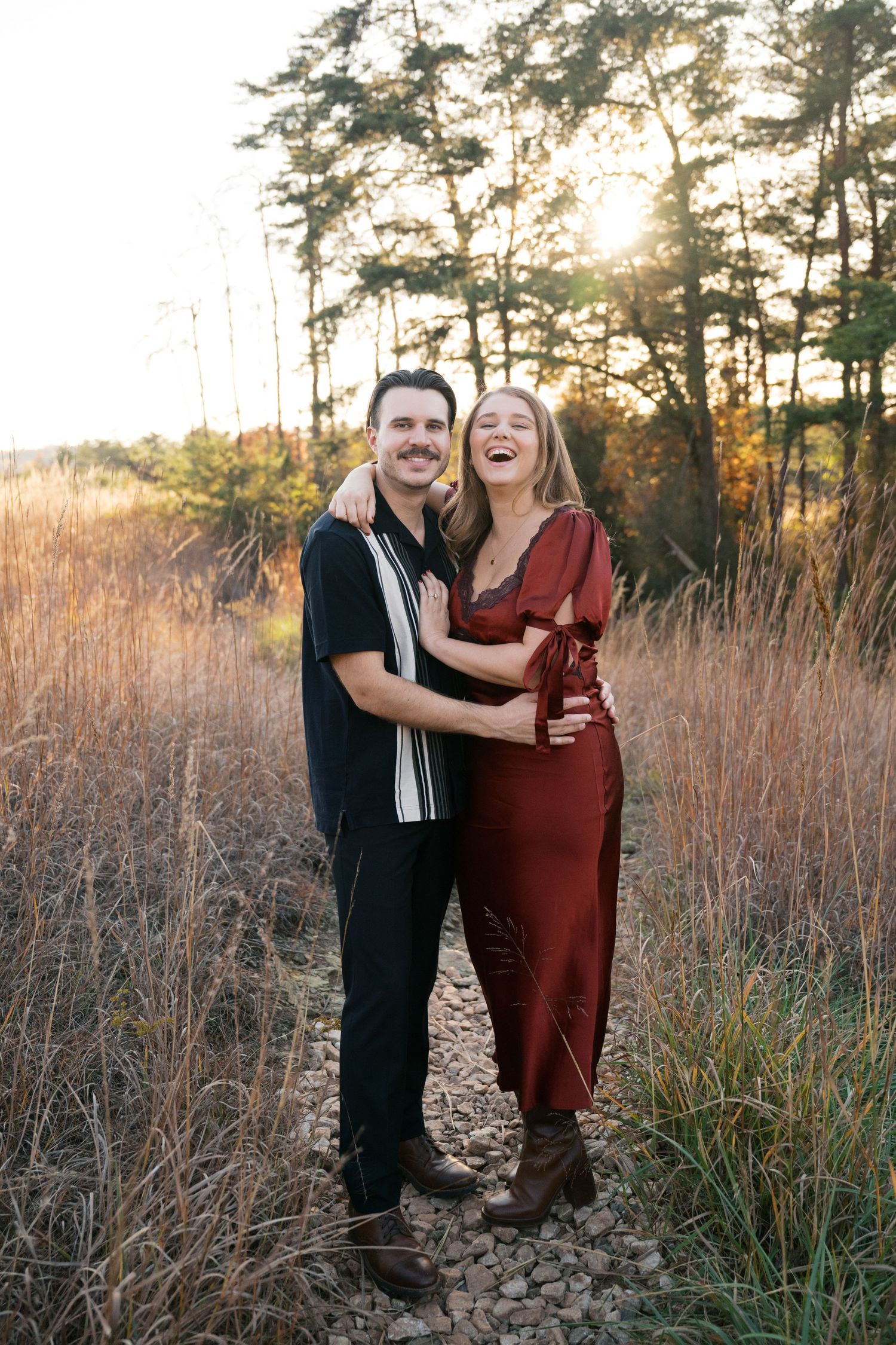 Couple sharing a joyful moment together at sunset in tall grass and pine trees.