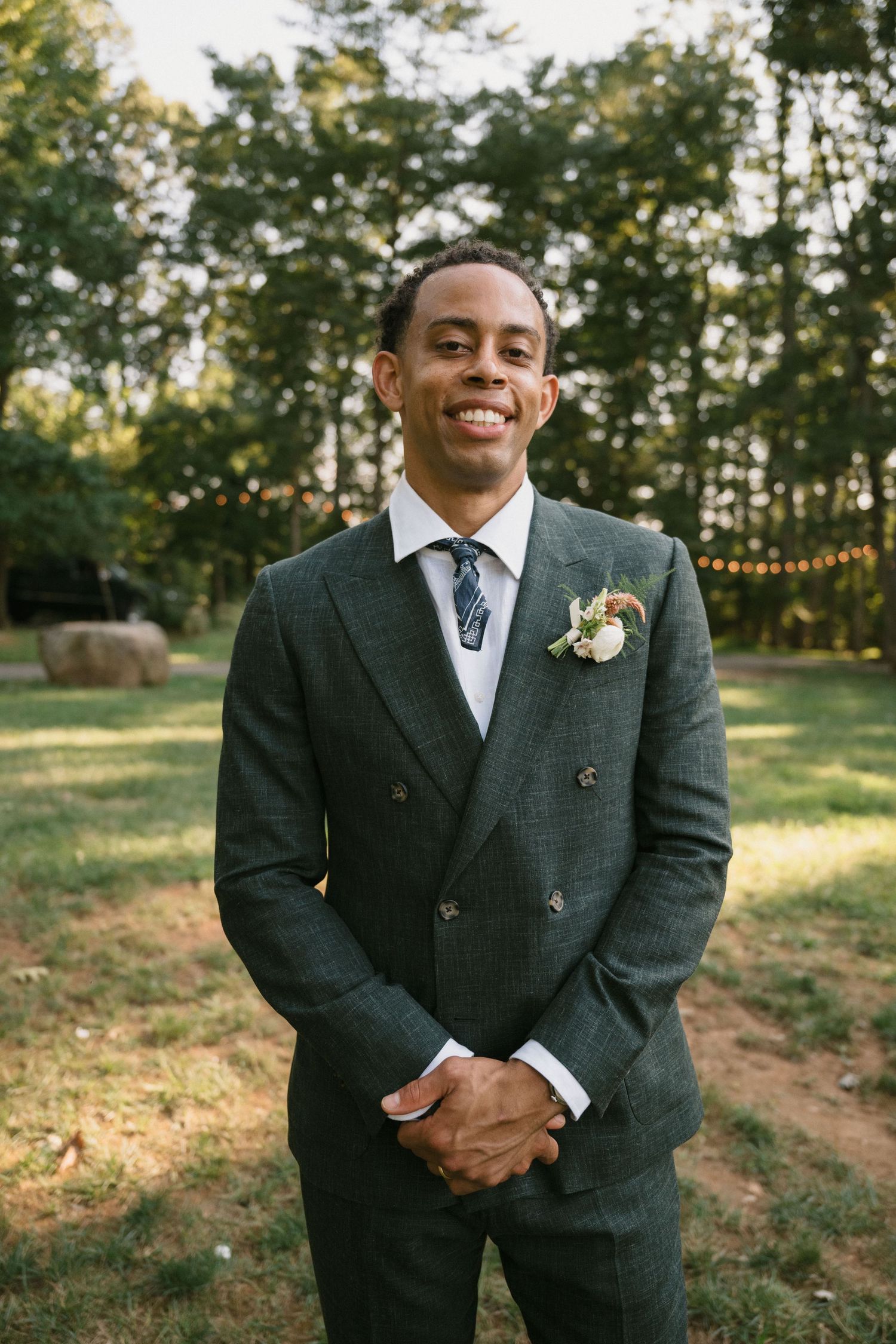 Groom in a stylish double-breasted suit poses in an outdoor garden setting.
