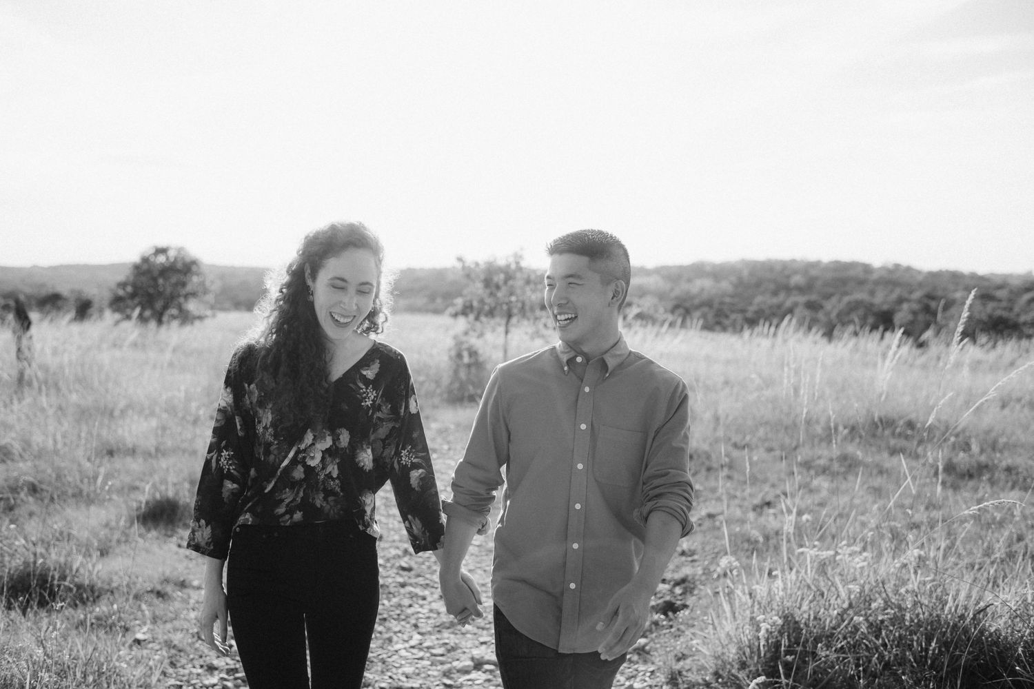 A couple walking together through a sunlit field in black and white.