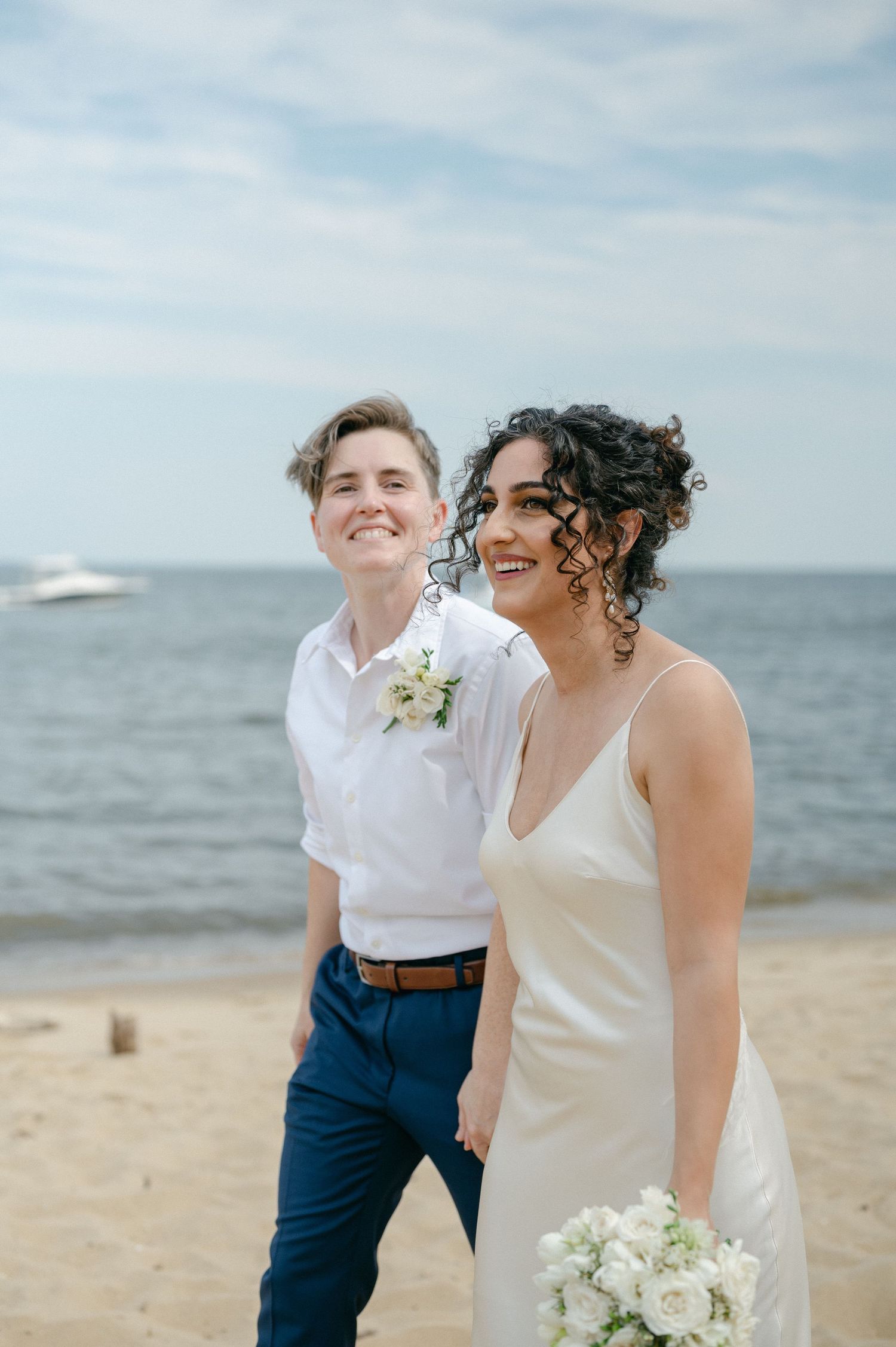 A happy couple shares joyful laughter together on a sunny beach with the ocean in the background.