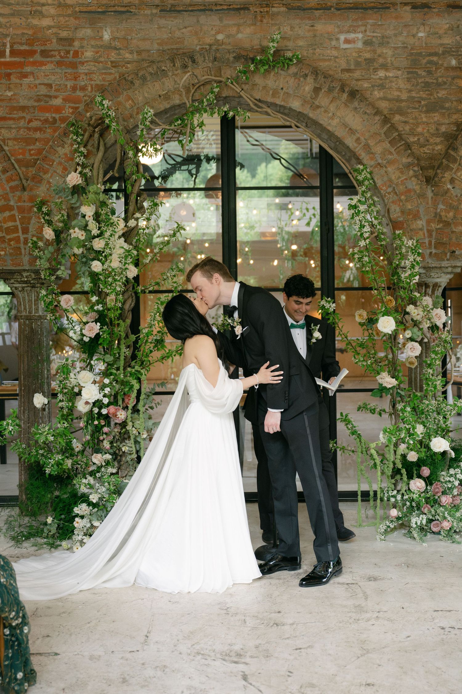 Wedding ceremony moment under a floral arch in a historic brick venue.