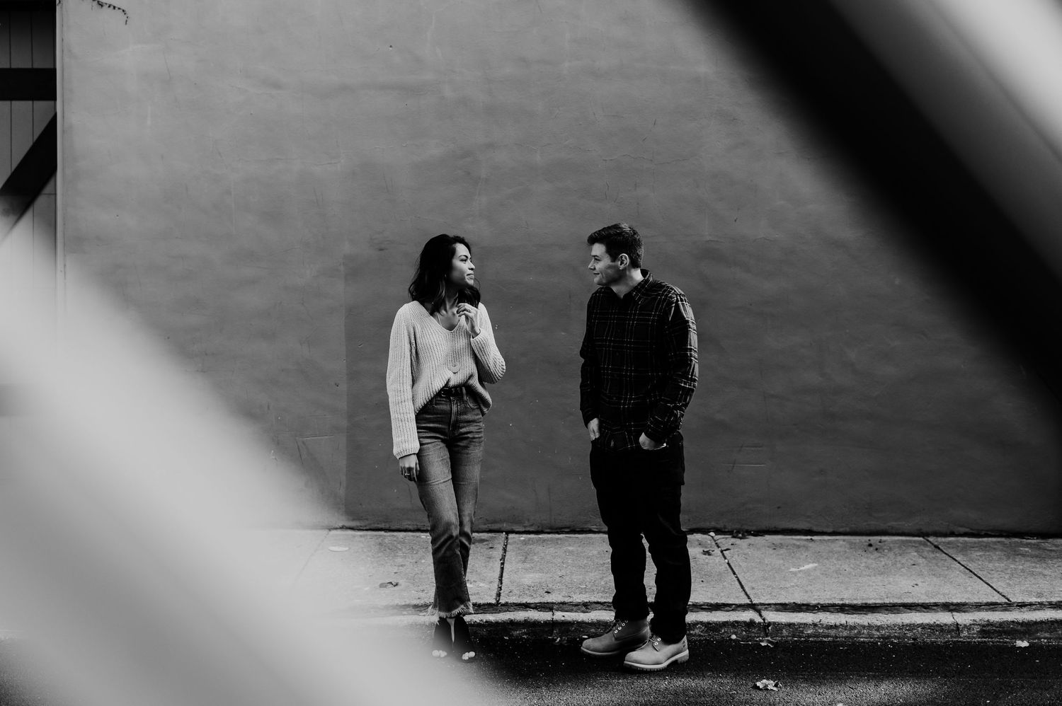 Black and white photo of a man and woman talking on a city sidewalk against a textured wall.