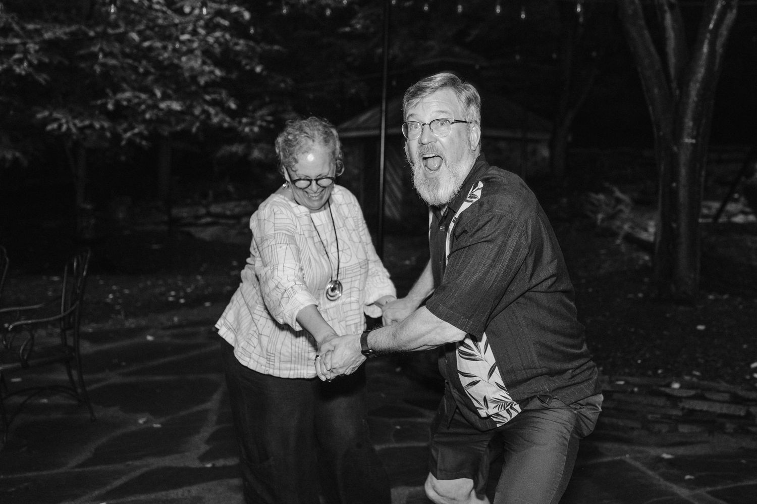 Black and white photo of two people dancing joyfully outdoors at night.