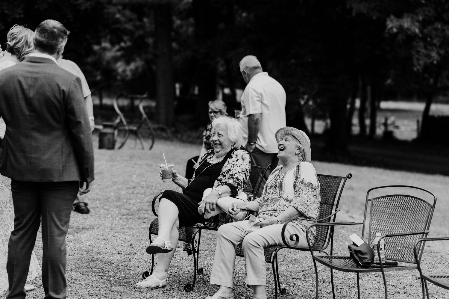 A black and white photo of wedding guests relaxing in outdoor chairs during a reception.