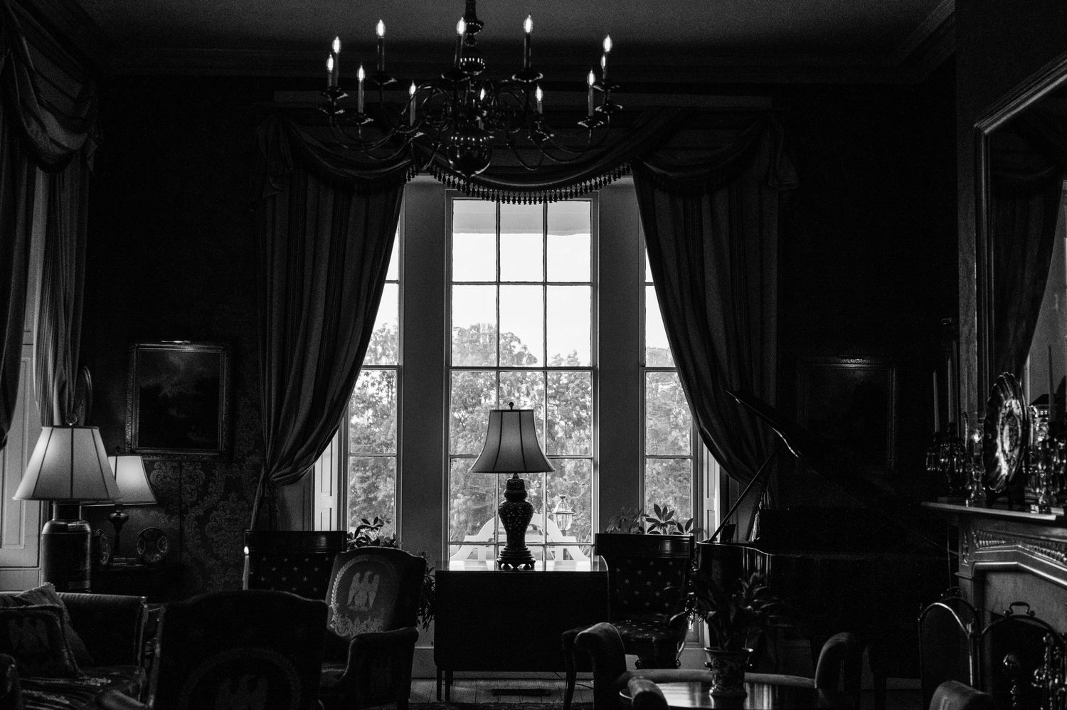 Elegant black and white interior with chandelier and large window framed by dramatic curtains.