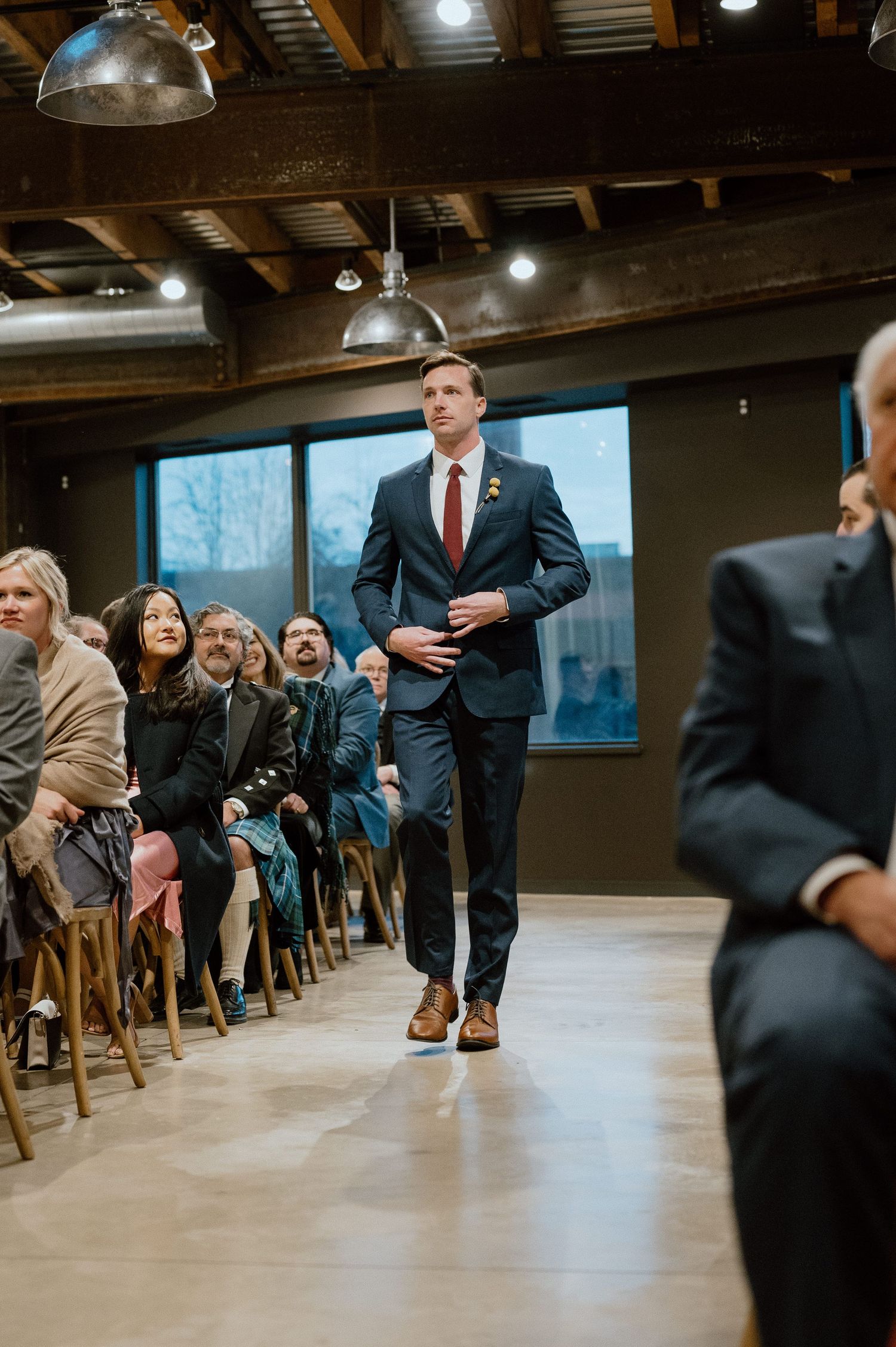 Formal event walkway with attendees seated along both sides in an industrial-style venue.