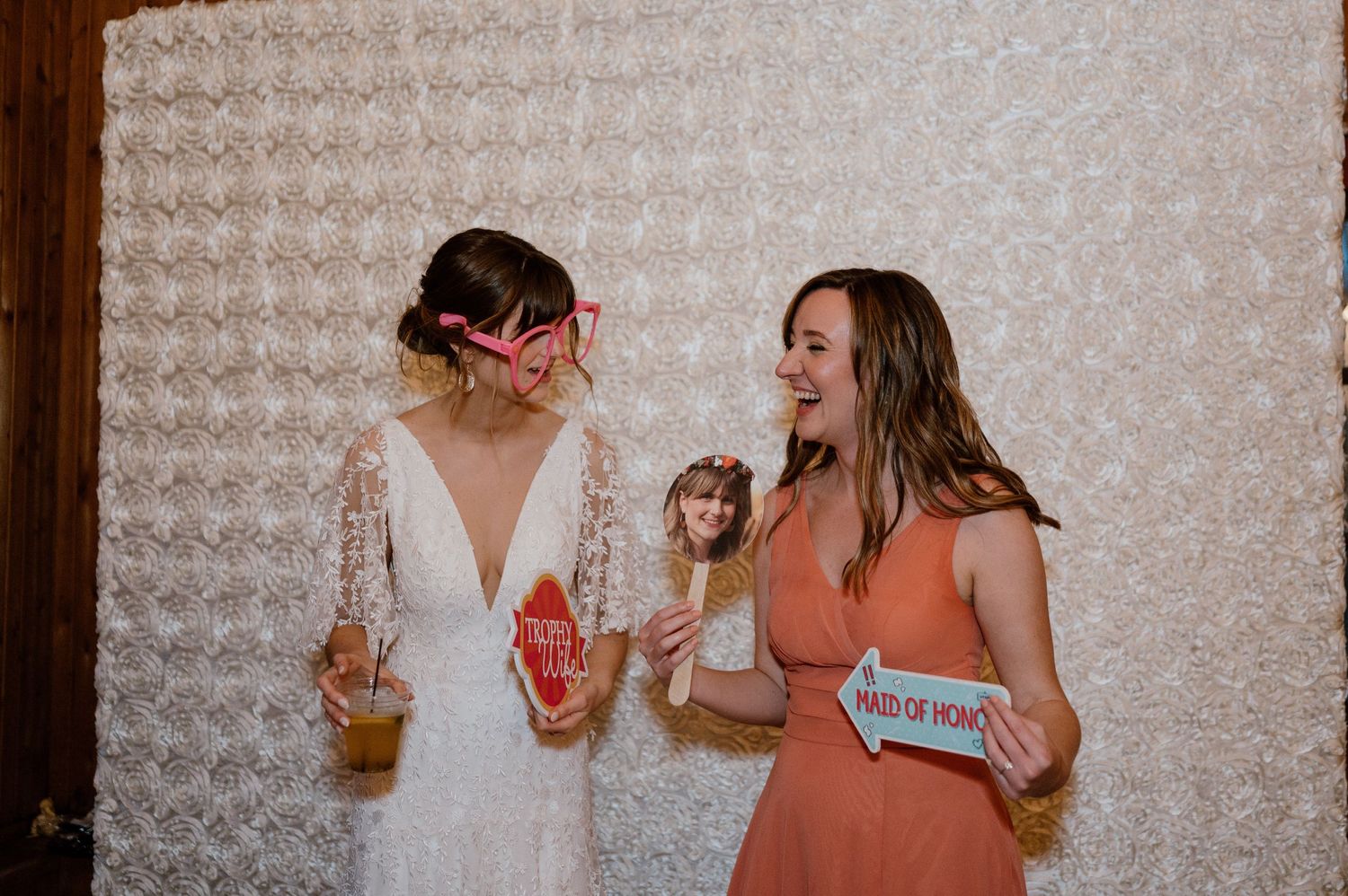 Two guests laughing and enjoying drinks at wedding photo booth.