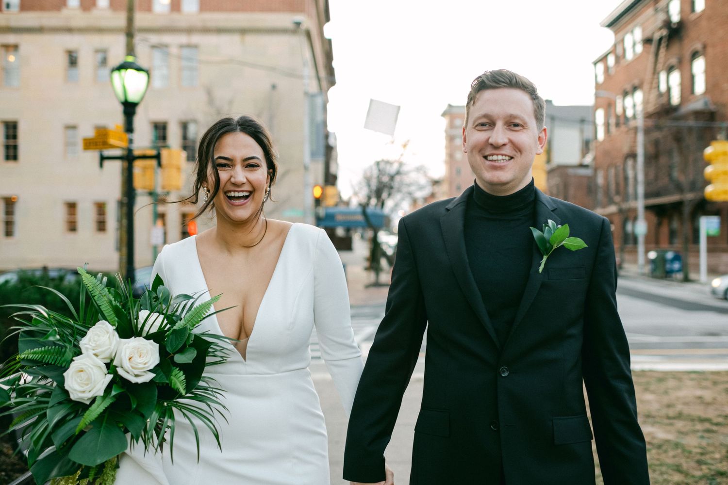 A newlywed couple shares laughter while walking together on a city street.