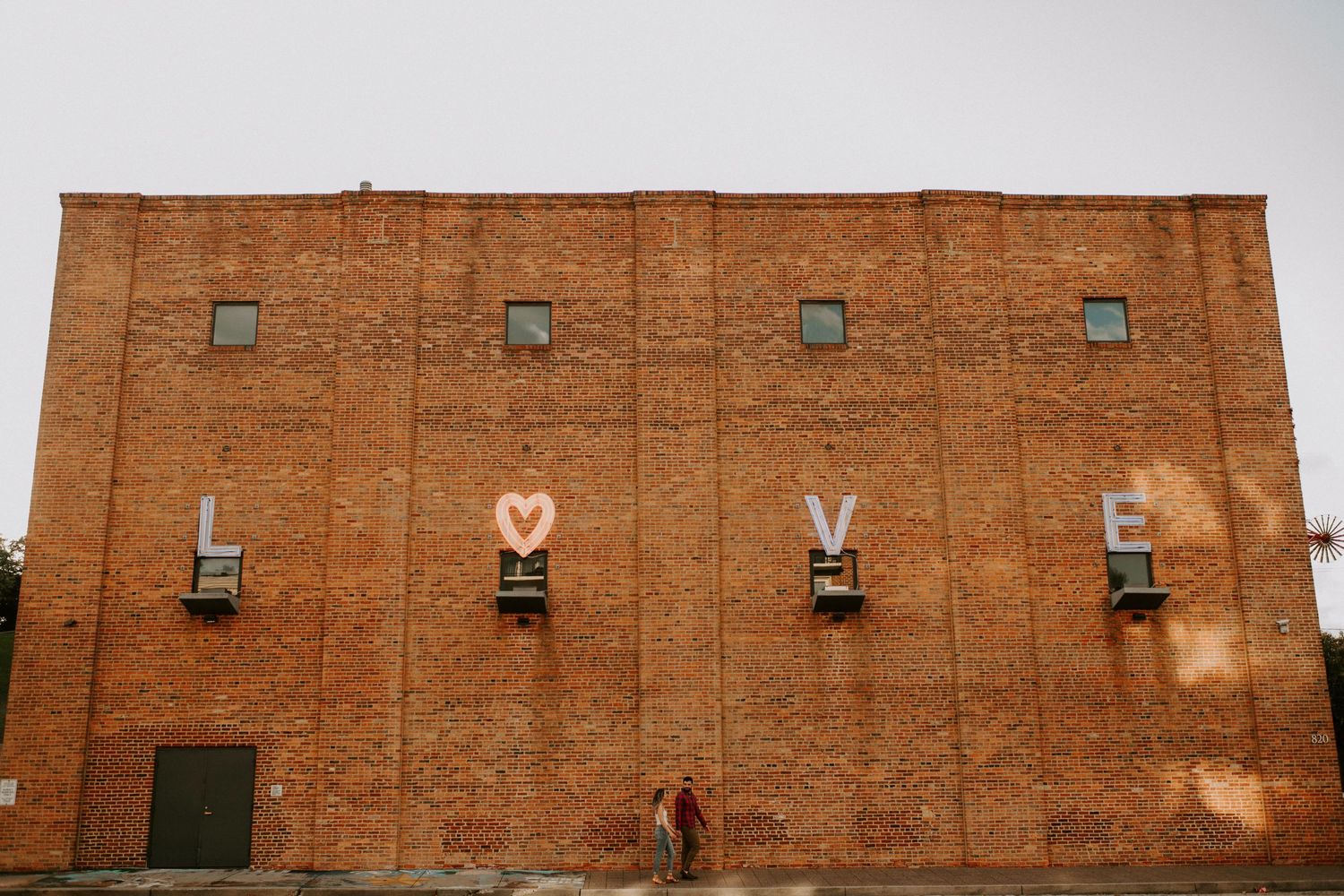 Large brick building facade with small windows and heart symbols painted below.